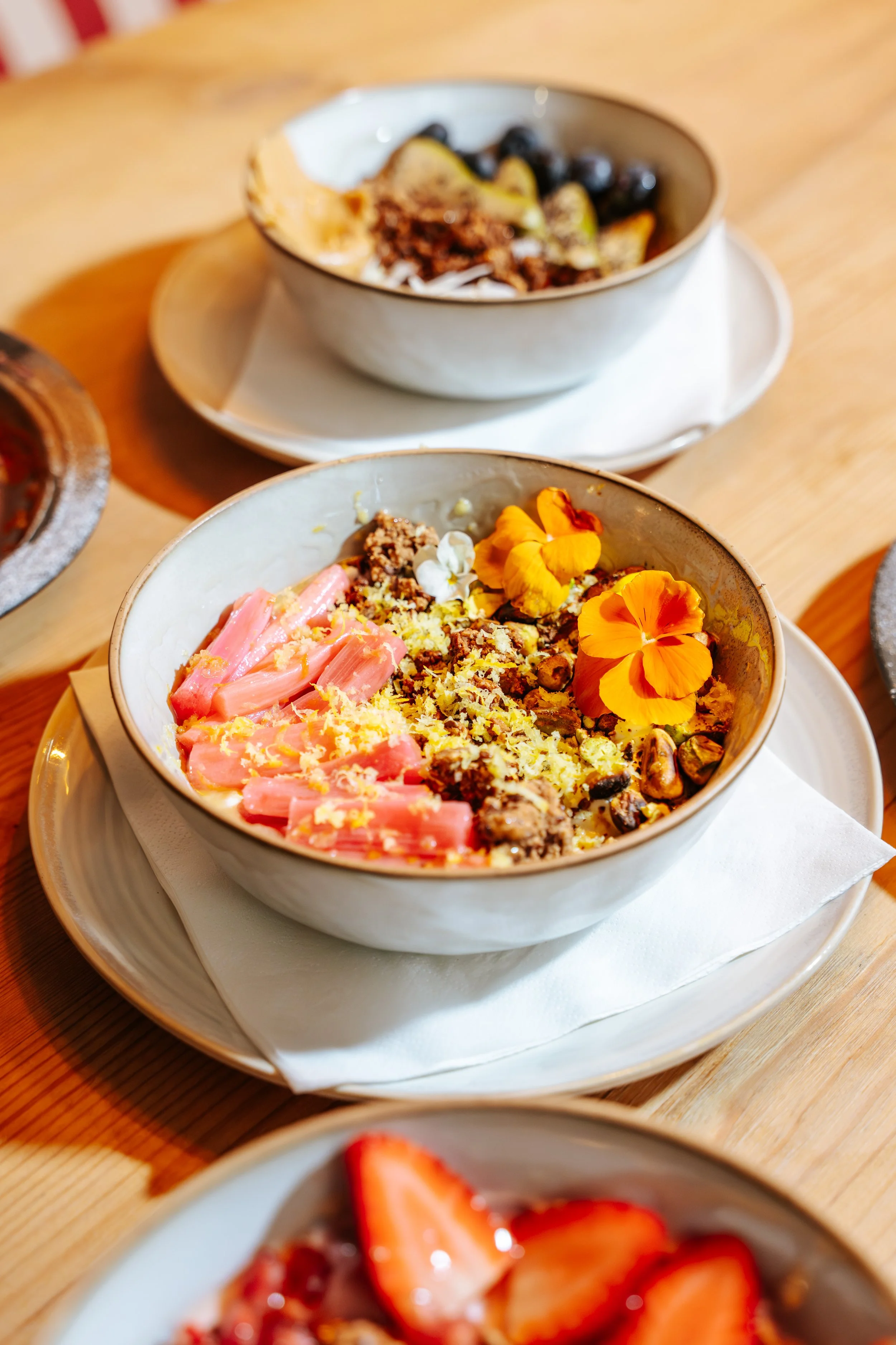 Bowls of colorful smoothie bowls topped with edible flowers, nuts, and granola on a wooden table.