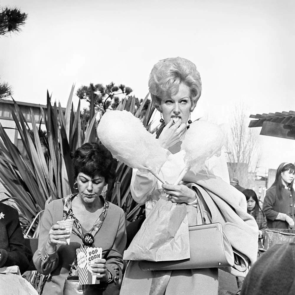 Photo of two well-dressed women. One eating popcorn and one eating cotton candy by Diane Arbus.