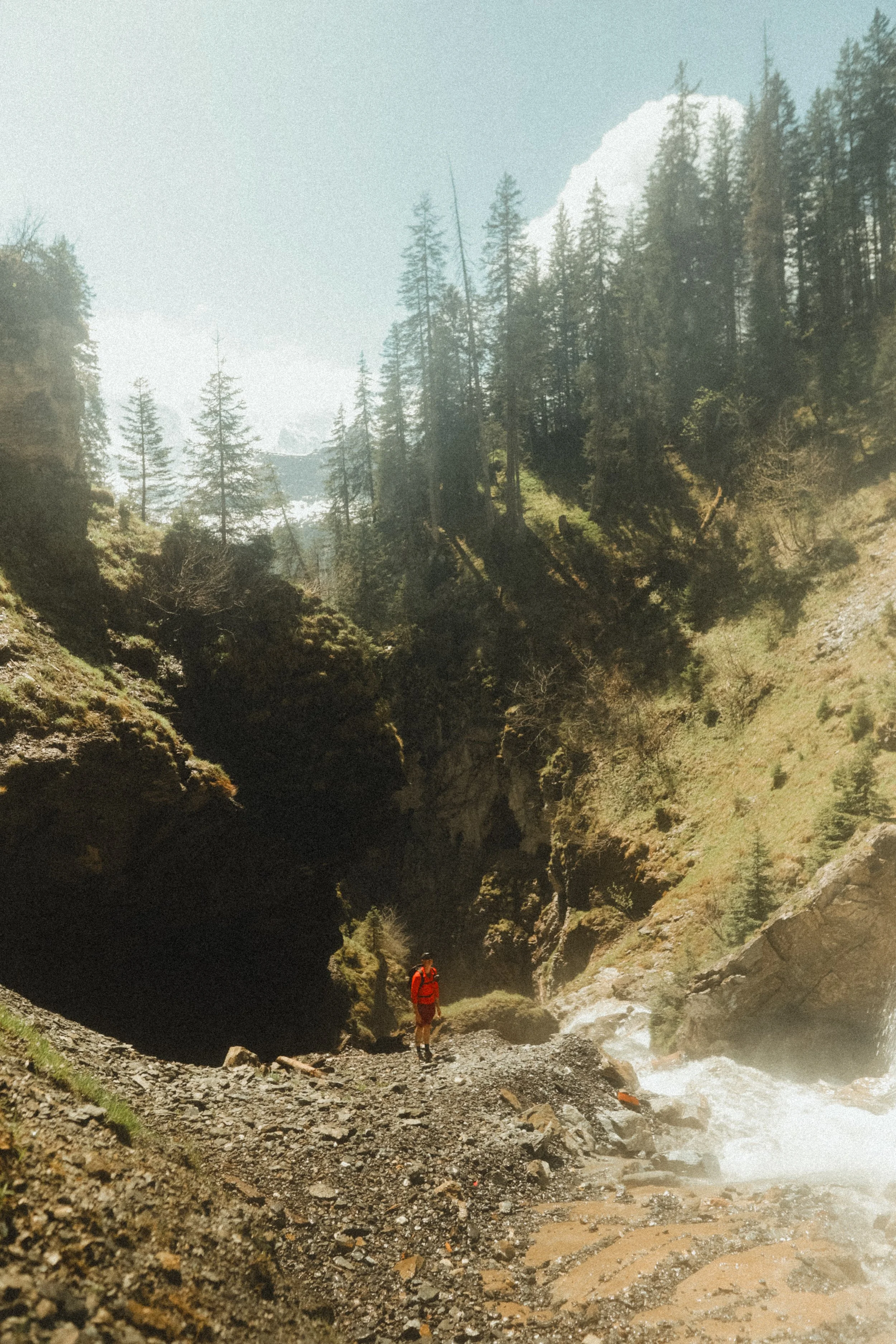 Hiker in red jacket walking on rocky trail right under Sprutz waterfall near Mürren, above the Lauterbrunnen Valley.