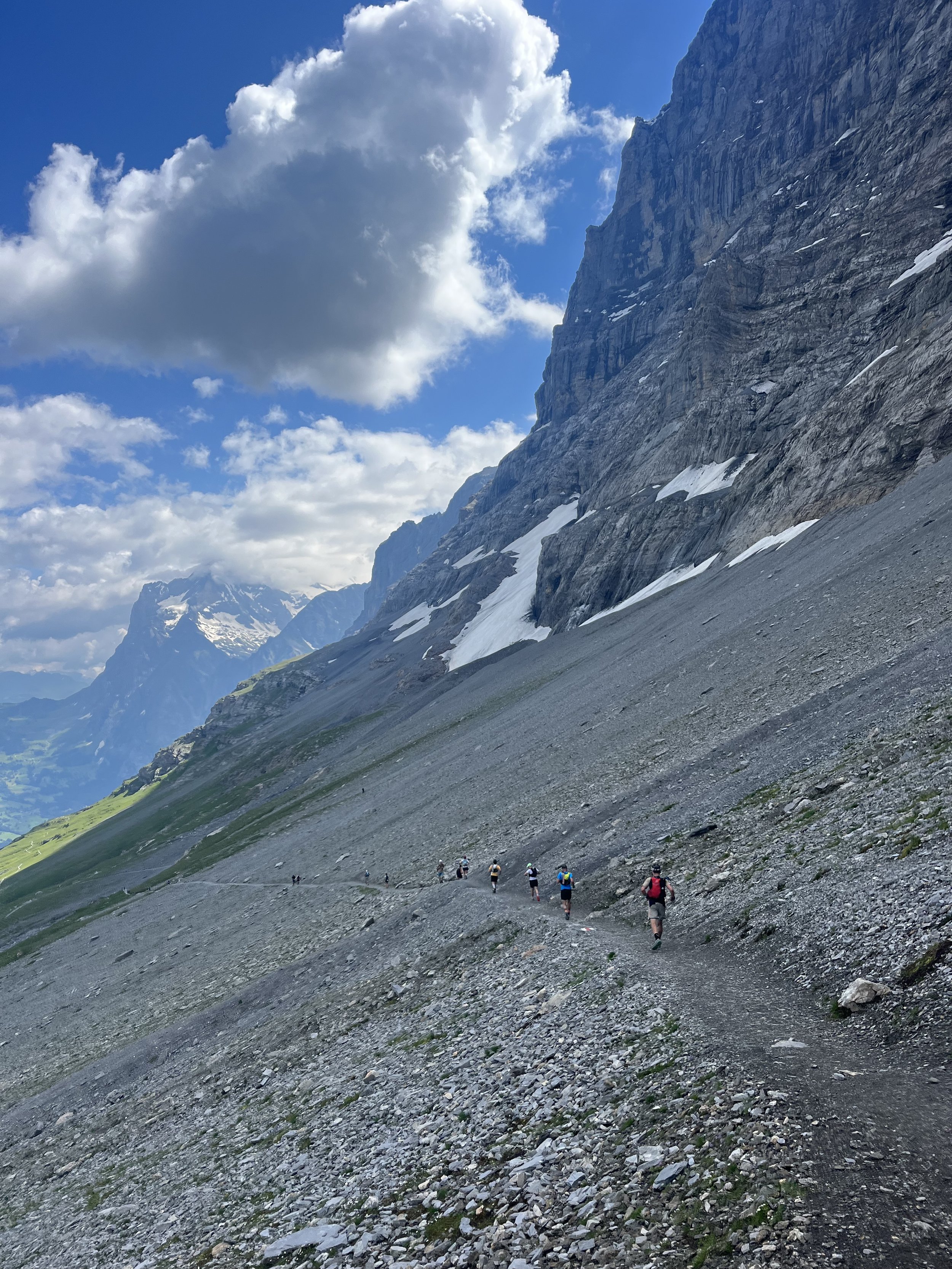 Hikers walking on a rocky mountain trail under a cloudy sky.