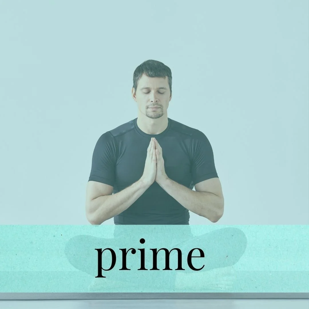 A man with short dark hair and a beard, eyes closed, hands pressed together in prayer or meditation, standing behind a table with the word 'prime' written on it.