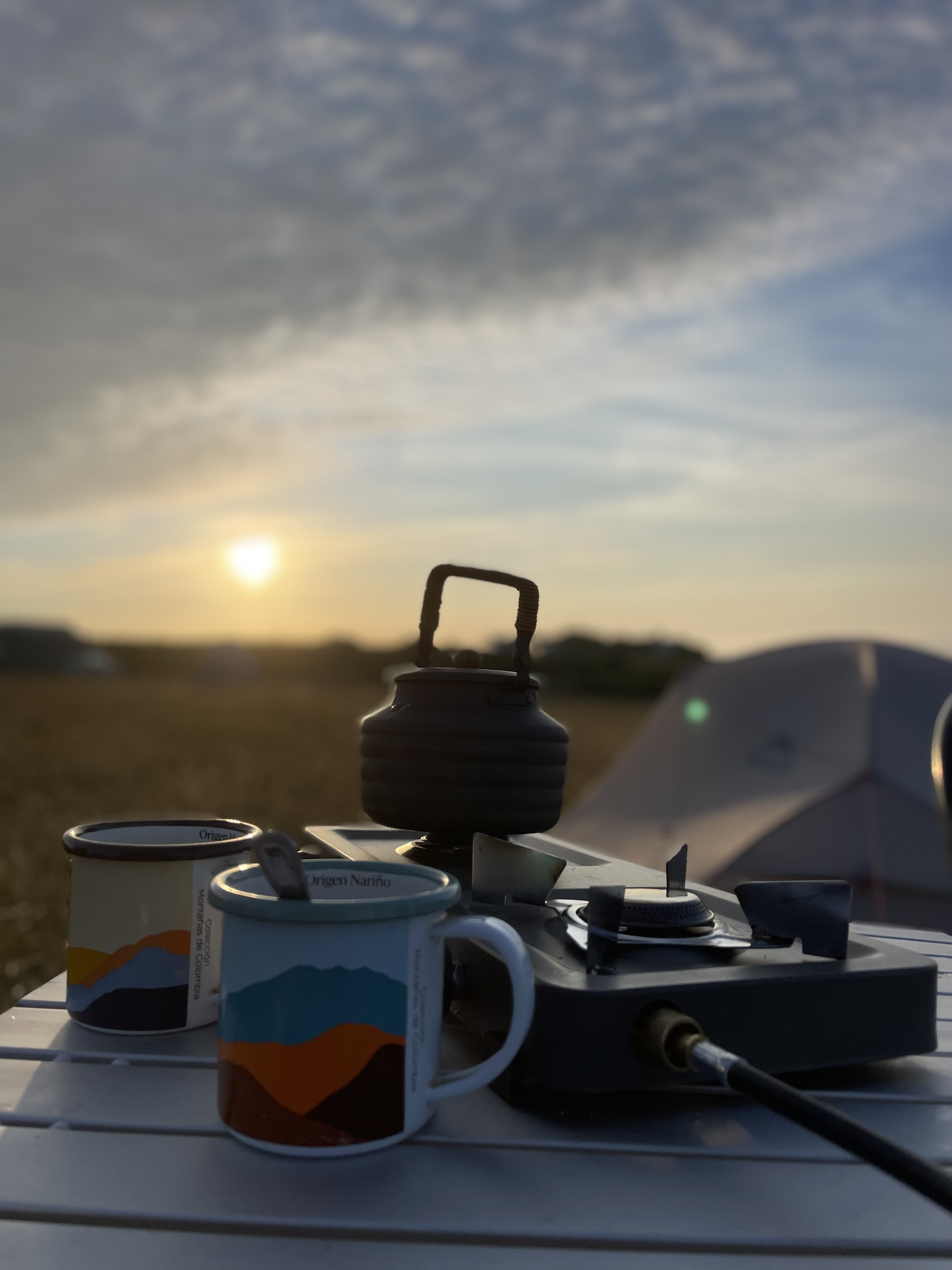 Camping and guided walk in East Prawle, South Devon.  Stove, kettle, and mugs on a table outdoors at sunset with a tent in the background.
