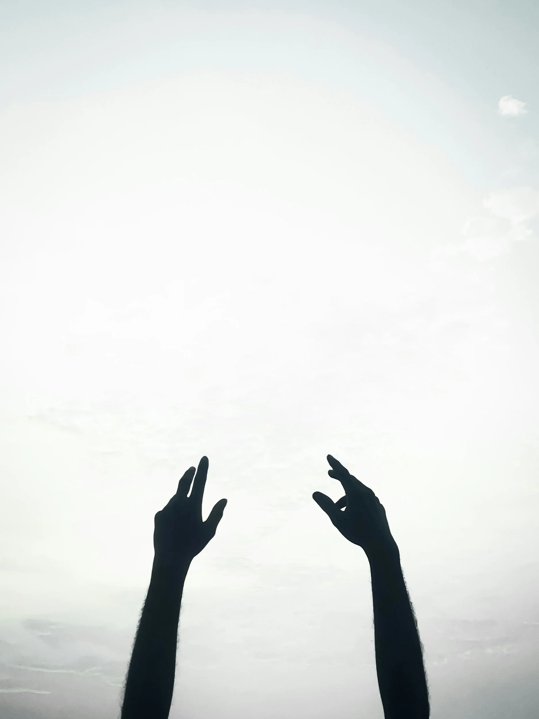 Silhouettes of two hands reaching towards the sky against a cloudy sky.