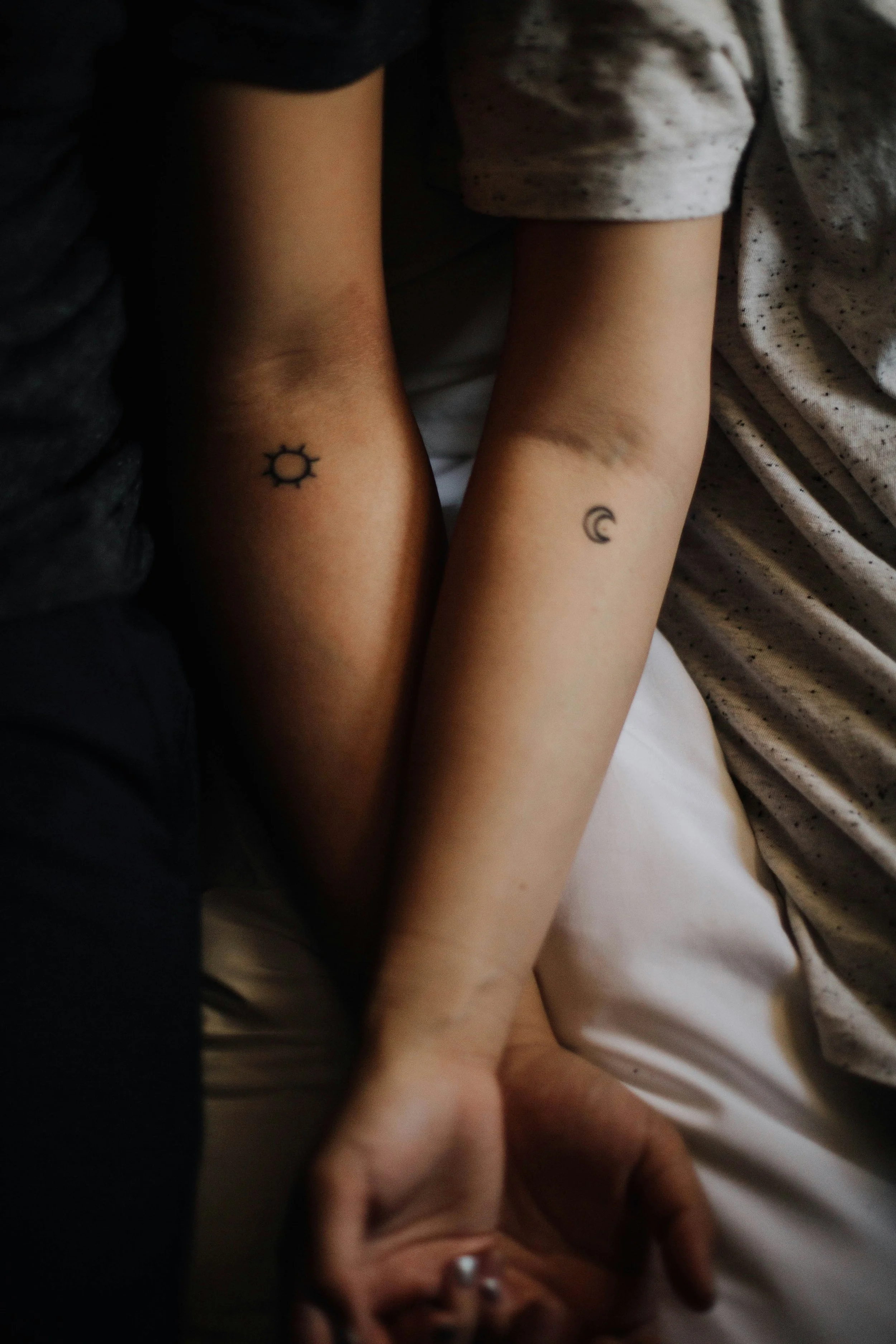Close-up of two children's arms with small tattoos, one with a sun symbol and the other with a crescent moon, lying closely with their other arms intertwined.