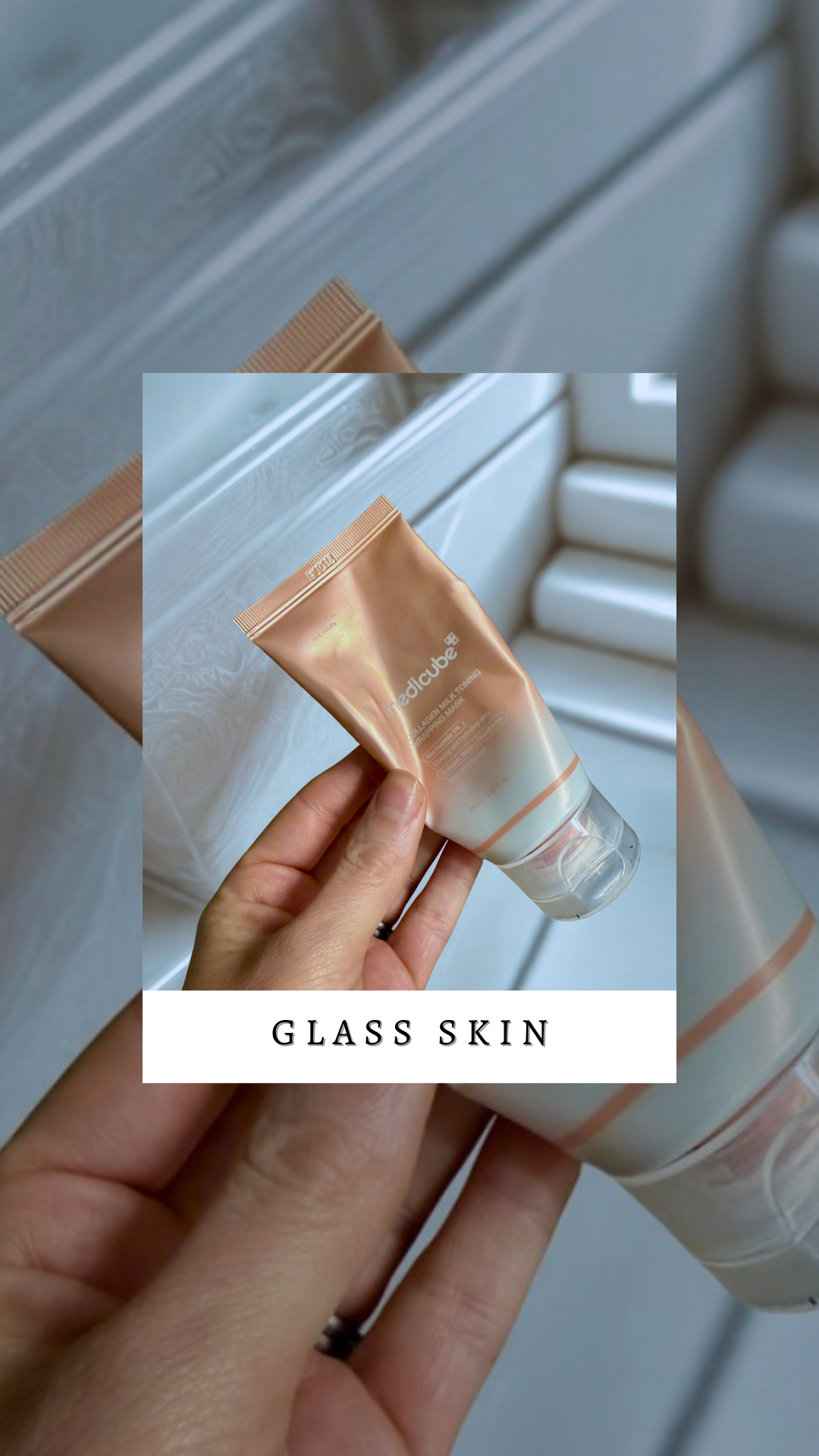 A hand holding a rose gold tube of MediCube Glass Skin Facial Milk Toning Mask in front of a frosted glass window.