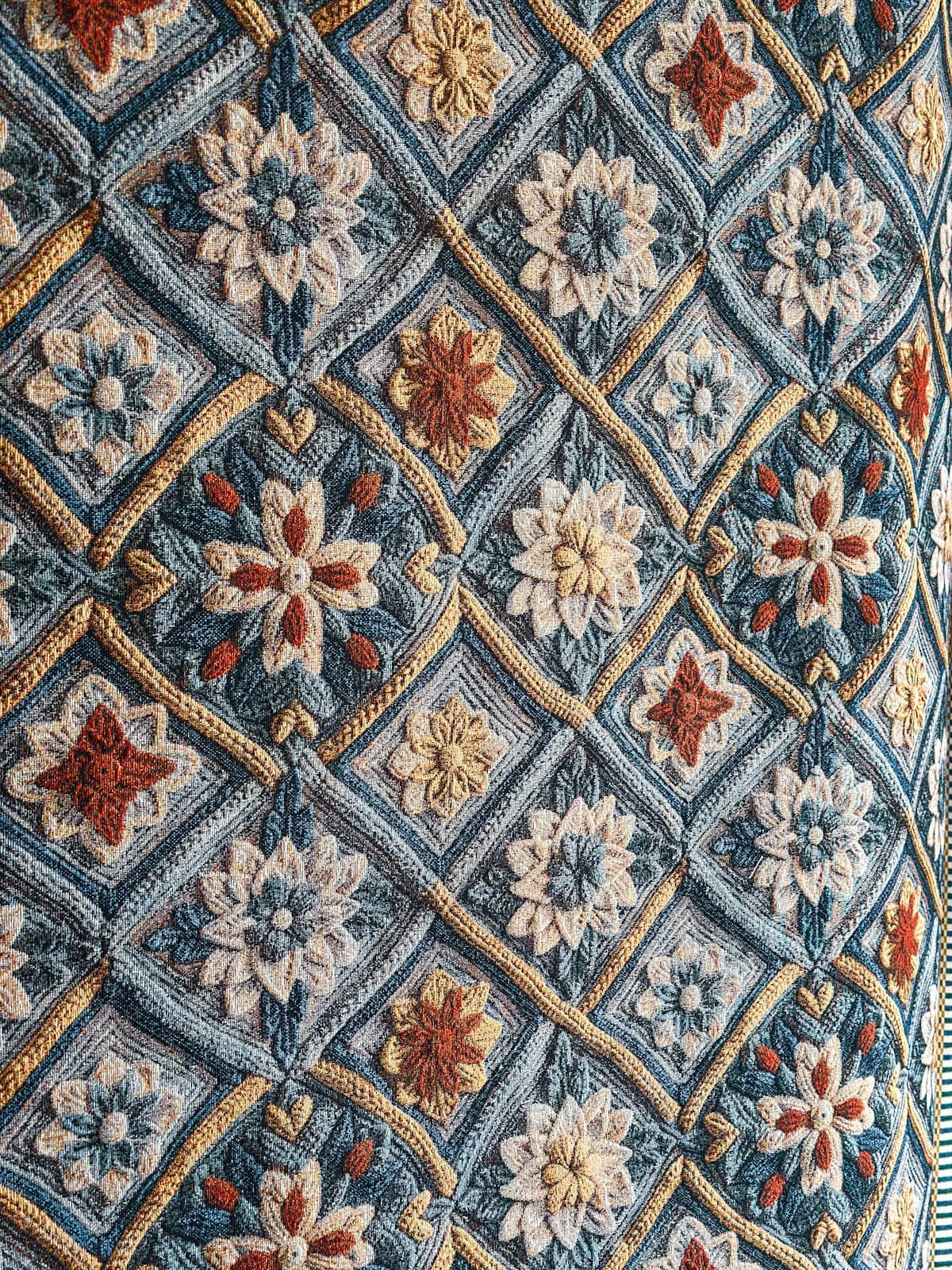 Tappeto tessuto con motivo floreale geometrico in tonalità di blu, beige, rosso e giallo.