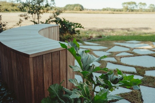 Tuin met houten bank en pad van keien in een landelijke omgeving.