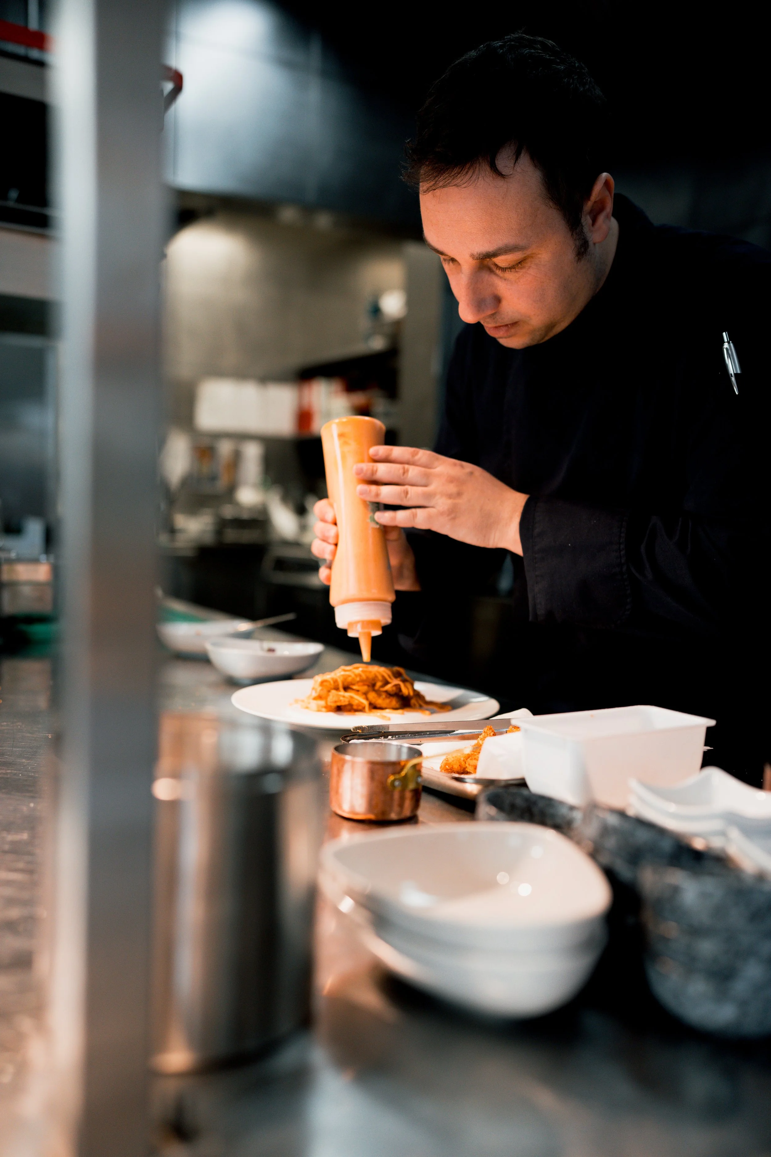 Chef preparing a dish on a kitchen counter, using a squeeze bottle for sauce.