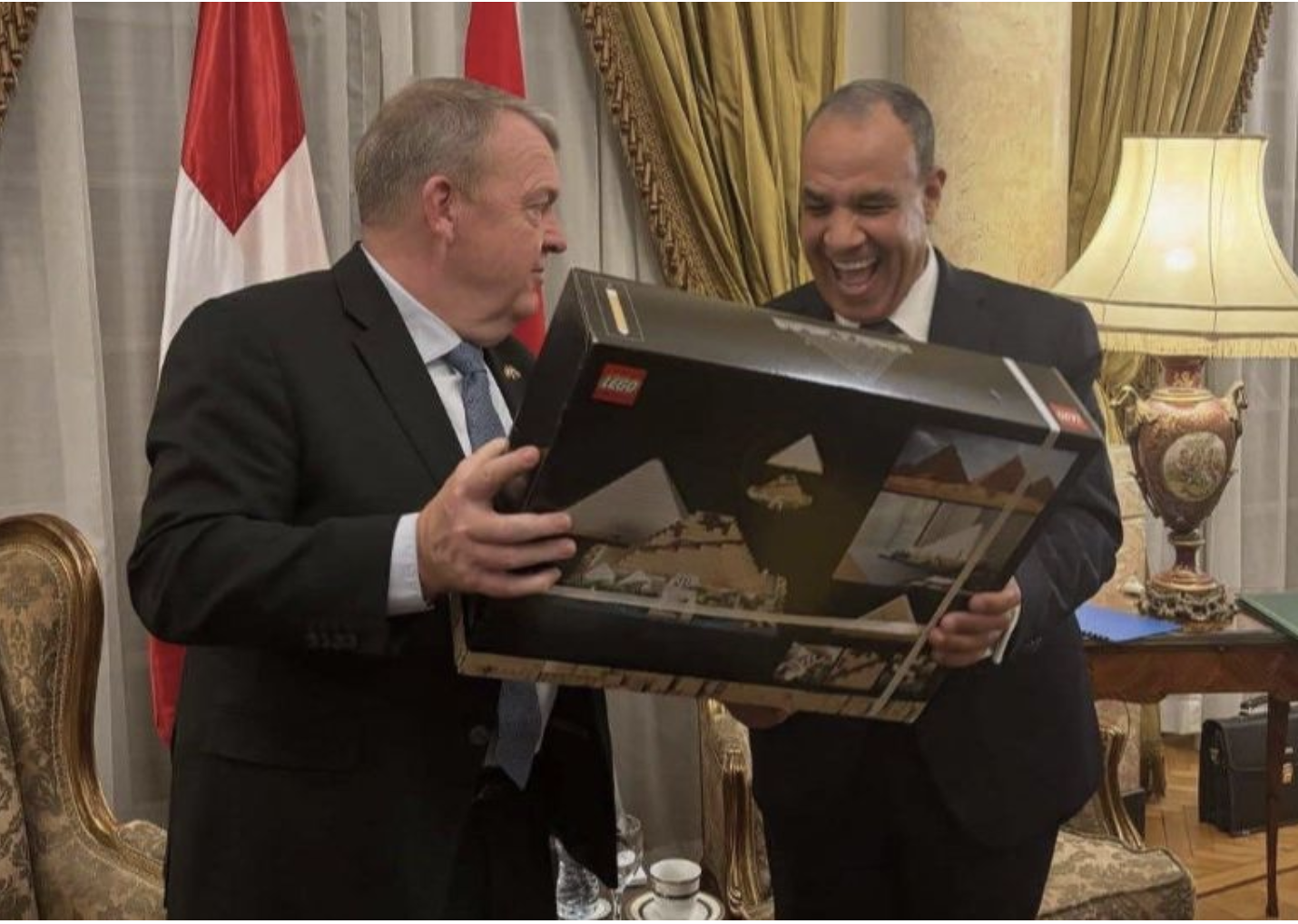 Danish and Egyptian Foreign Ministers share a laugh over a symbolic LEGO Great Pyramid gift during the 2025 Grand Egyptian Museum opening, illustrating narrative-driven diplomatic protocol.