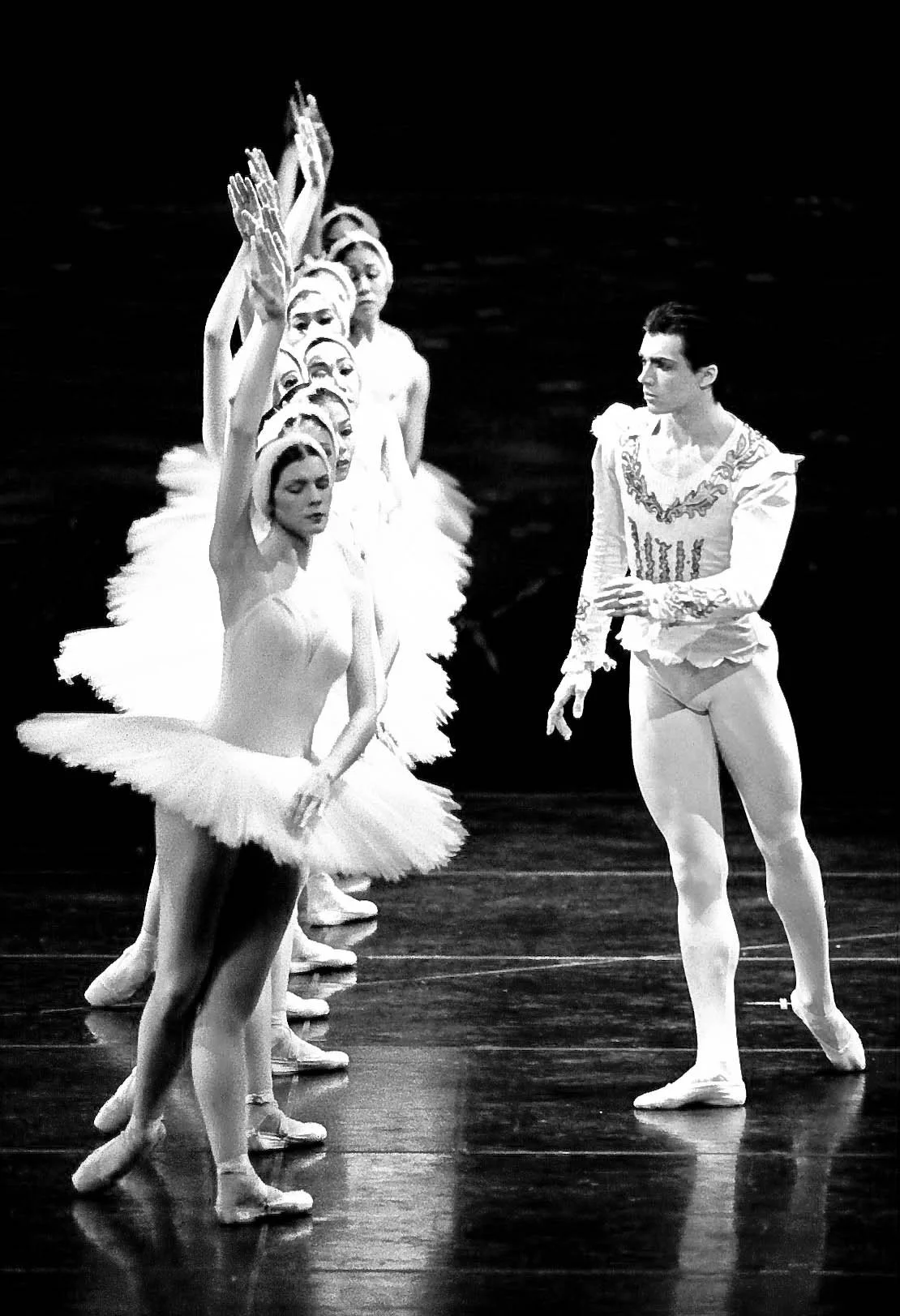 Ballet dancers in tutus and a male dancer in a costume during a performance on stage in black and white. Swan Lake
