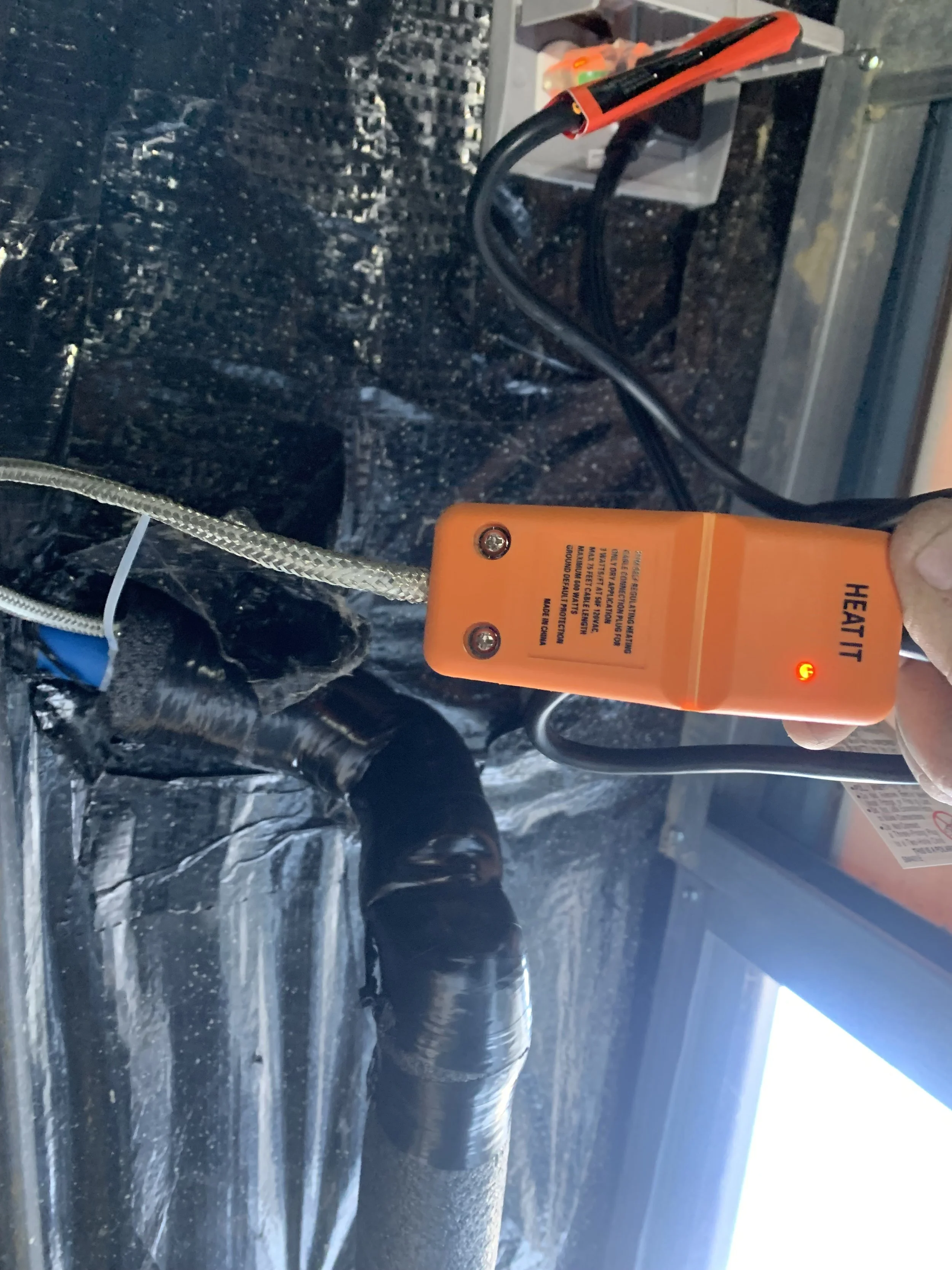 A person holding an orange heat tape plug that heats the main water line that feeds into the mobile home underbelly.