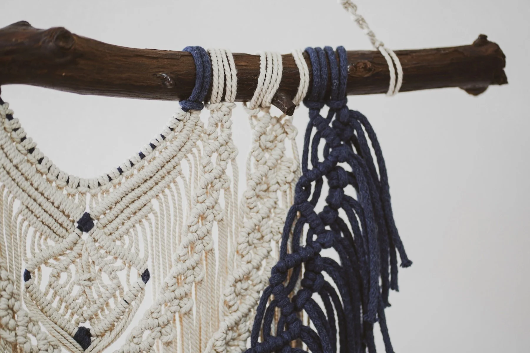 Macramé wall hangings in cream and navy blue colors hanging on a wooden rod.