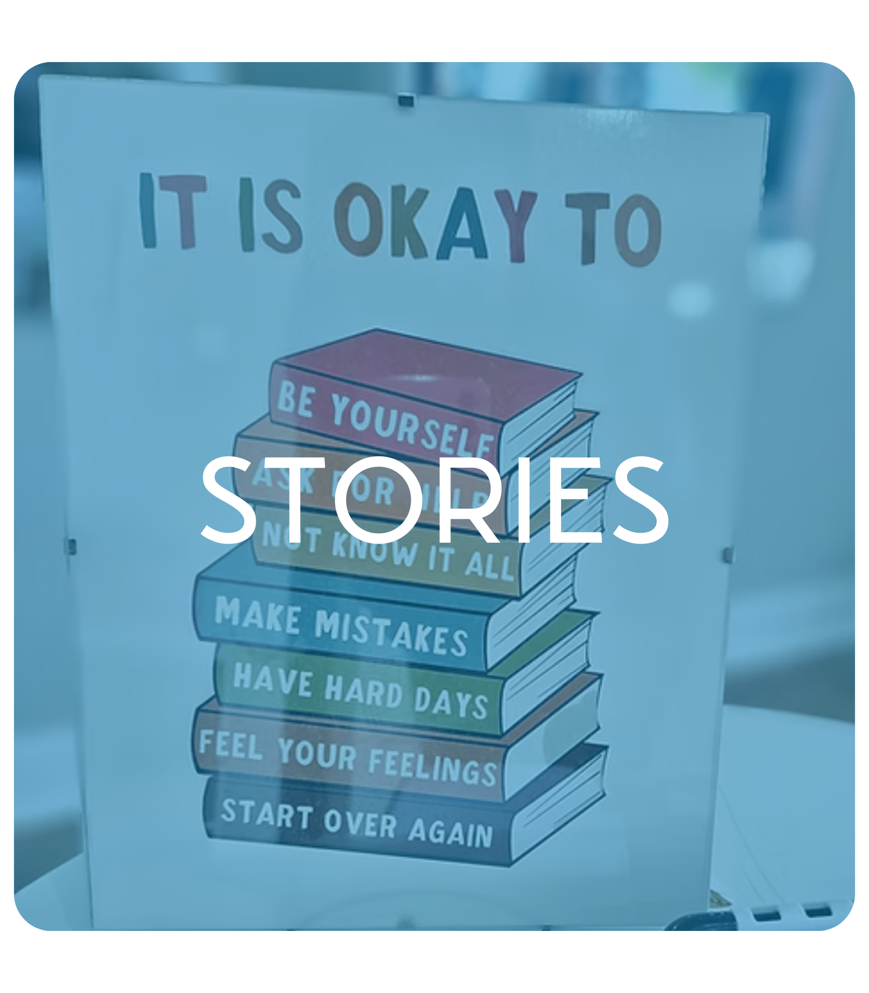 Sign with stacked books labeled "It is okay to: Be Yourself, Not Know It All, Make Mistakes, Have Hard Days, Feel Your Feelings, Start Over Again," with overlay text "Stories."