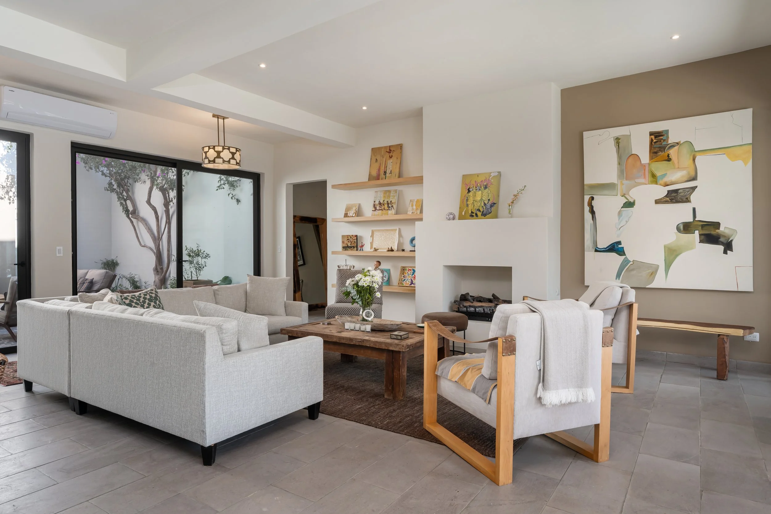 Modern living room with gray sectional sofa, armchair, wooden coffee table, large abstract painting, and built-in fireplace.