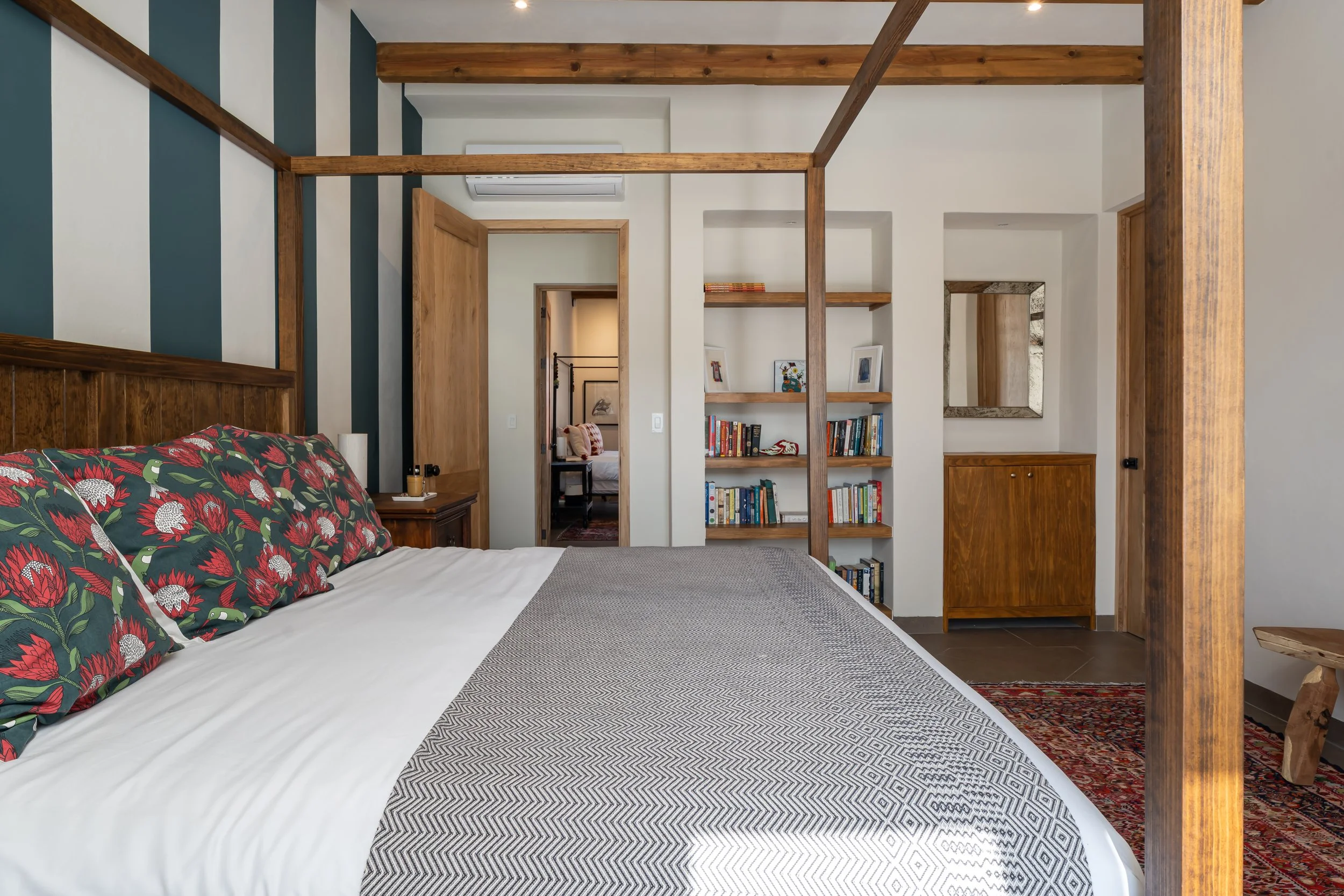 A bedroom with a four-poster bed, decorative pillows with a floral pattern, and a bookshelf with books and framed photos.