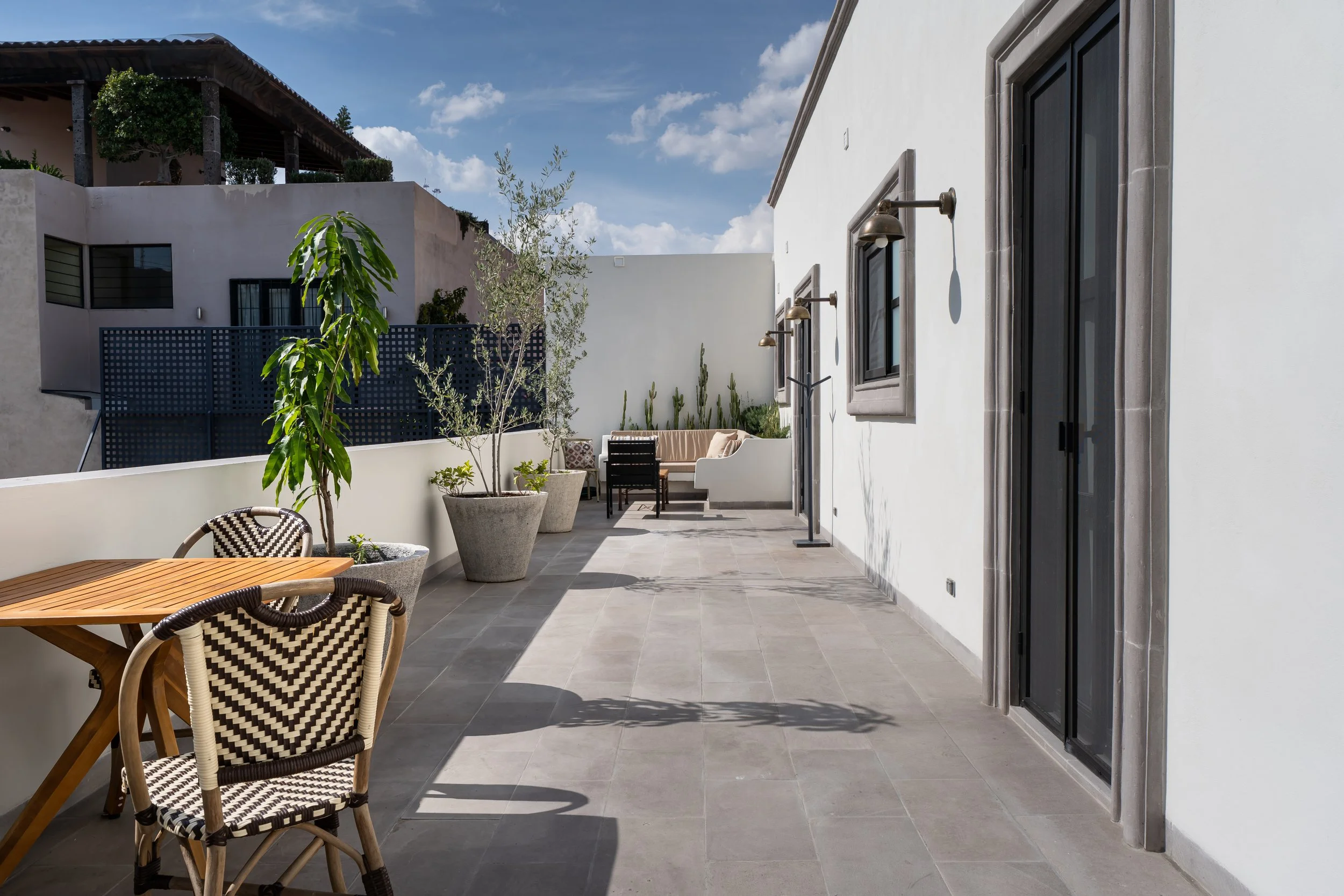 Outdoor terrace with patio furniture, potted plants, and wall-mounted lights under a partly cloudy sky.