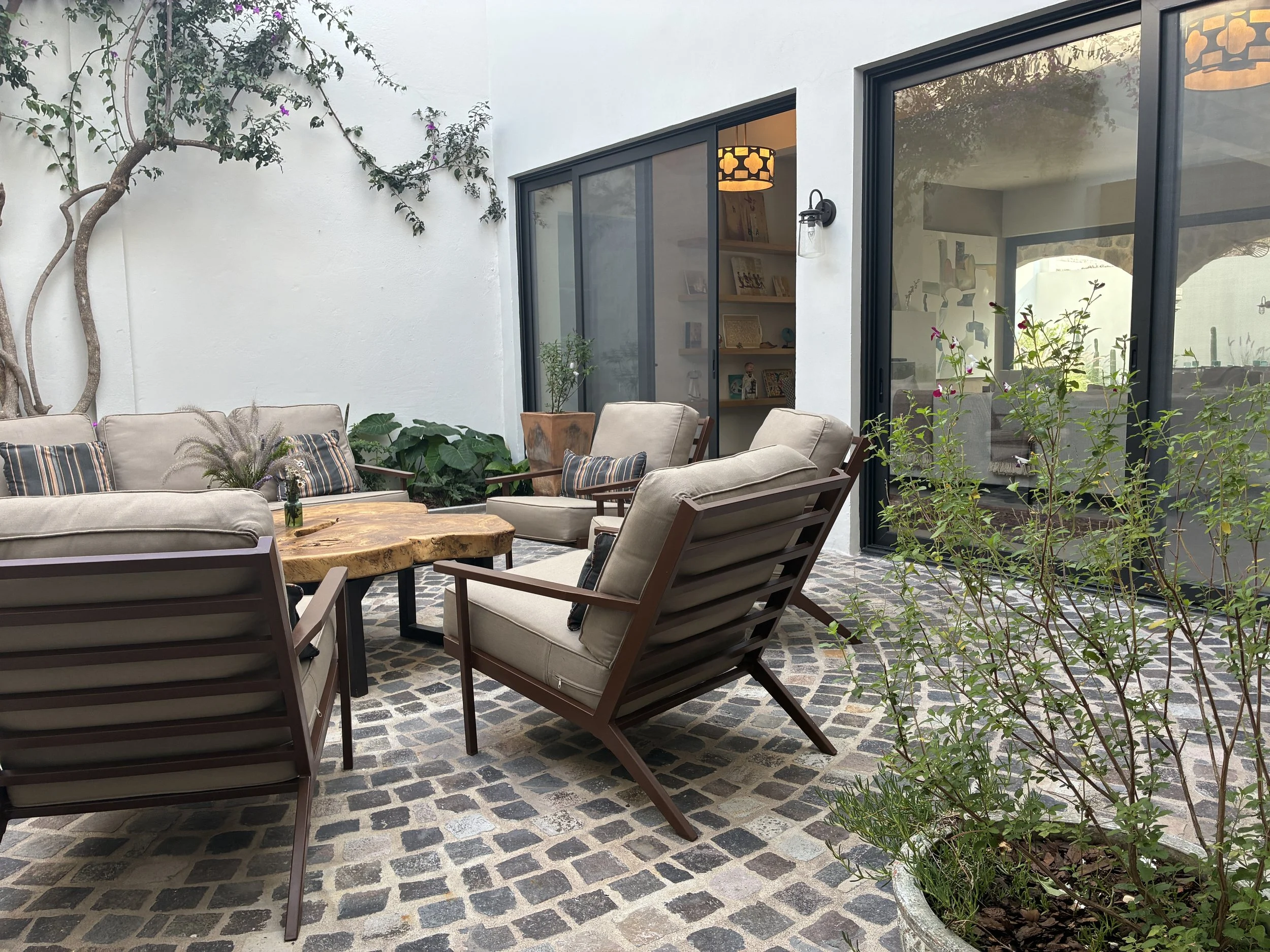 Outdoor patio with beige cushioned seating, a wooden coffee table, potted plants, and large glass sliding doors leading indoors.