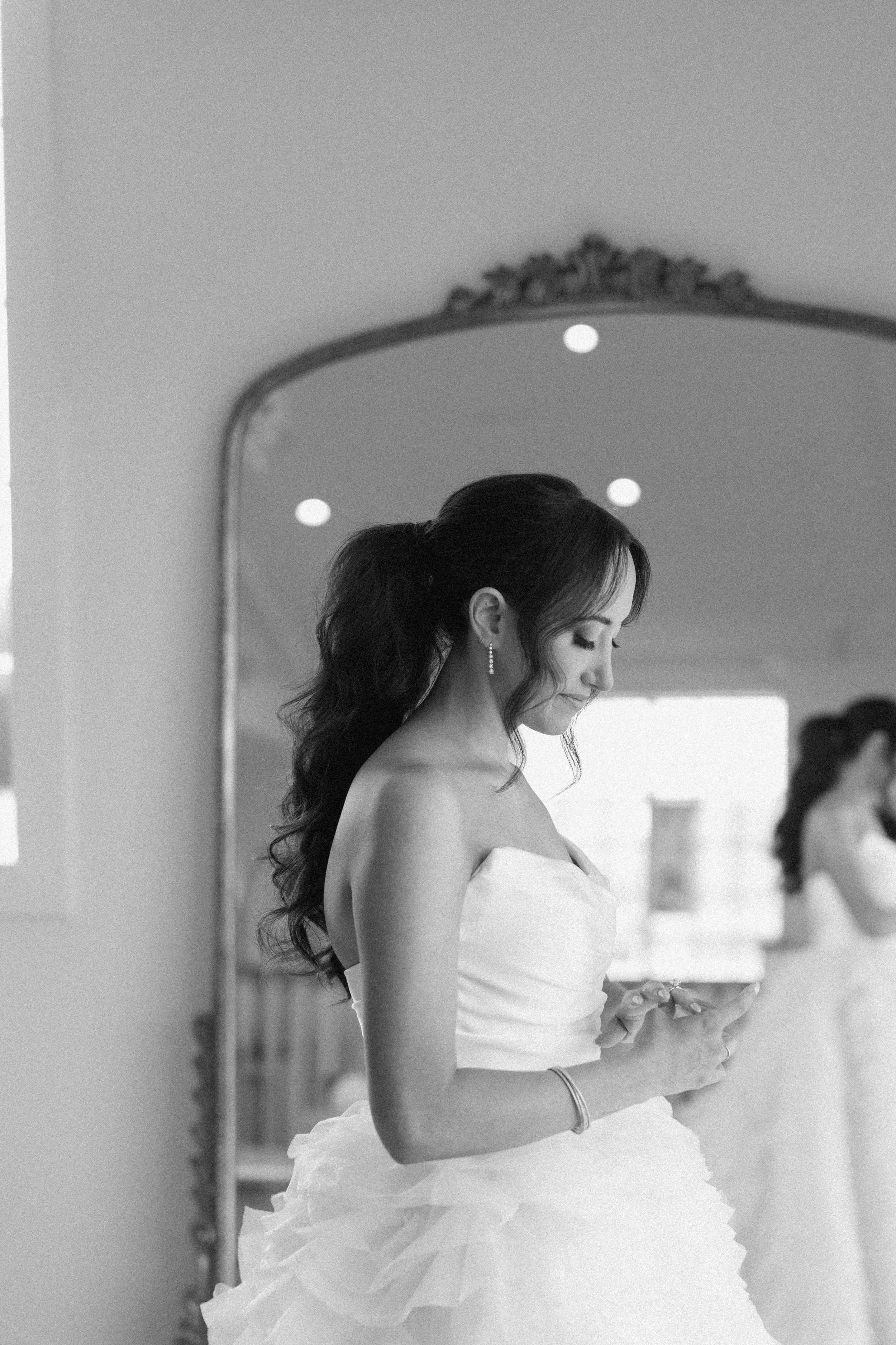 A woman in a wedding dress looking at her phone in front of a mirror.