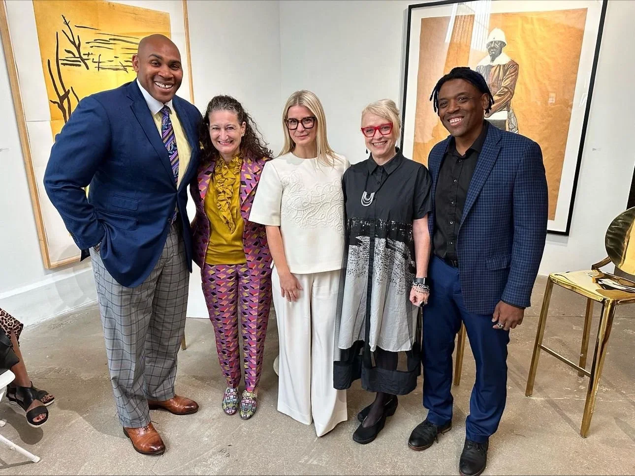 Five people standing together in an art gallery, smiling for a photo, with abstract artwork on the walls behind them.