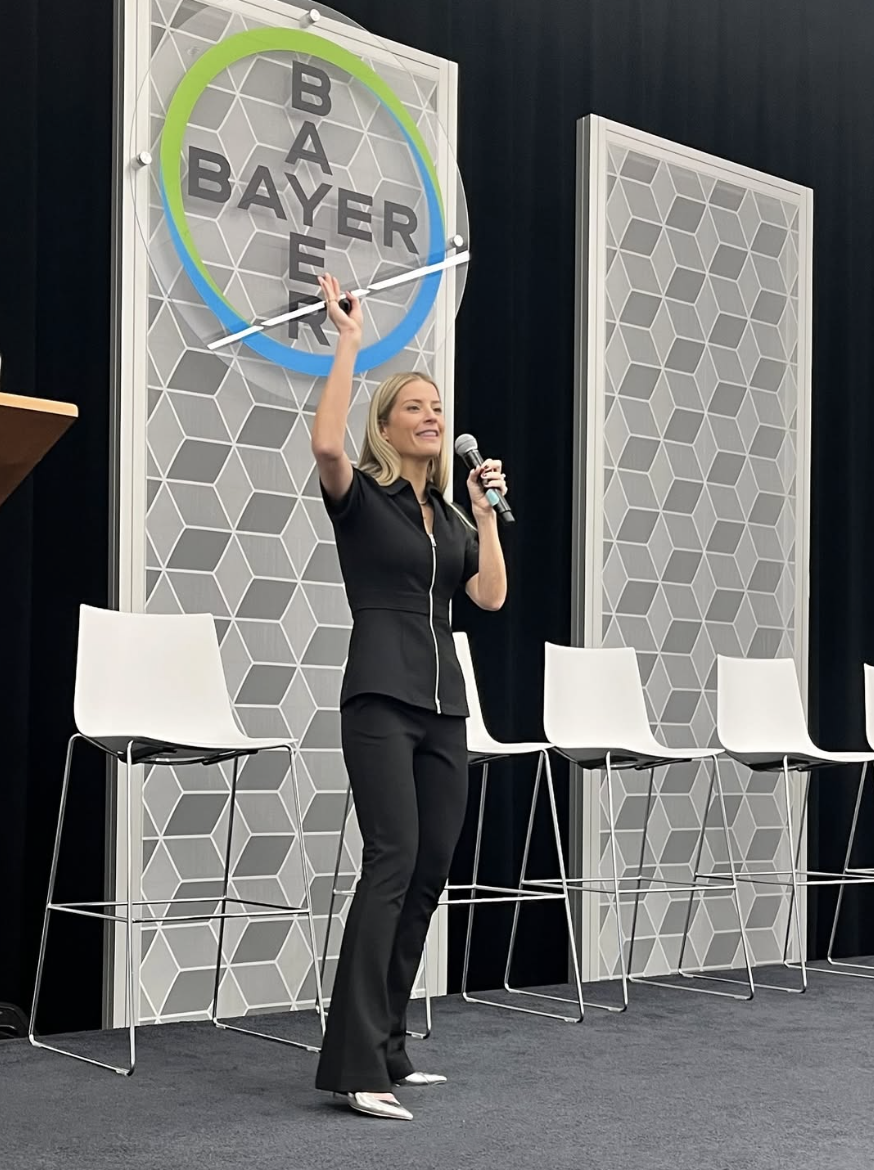 Laura K. Sawyier is standing on a stage speaking at Bayer.