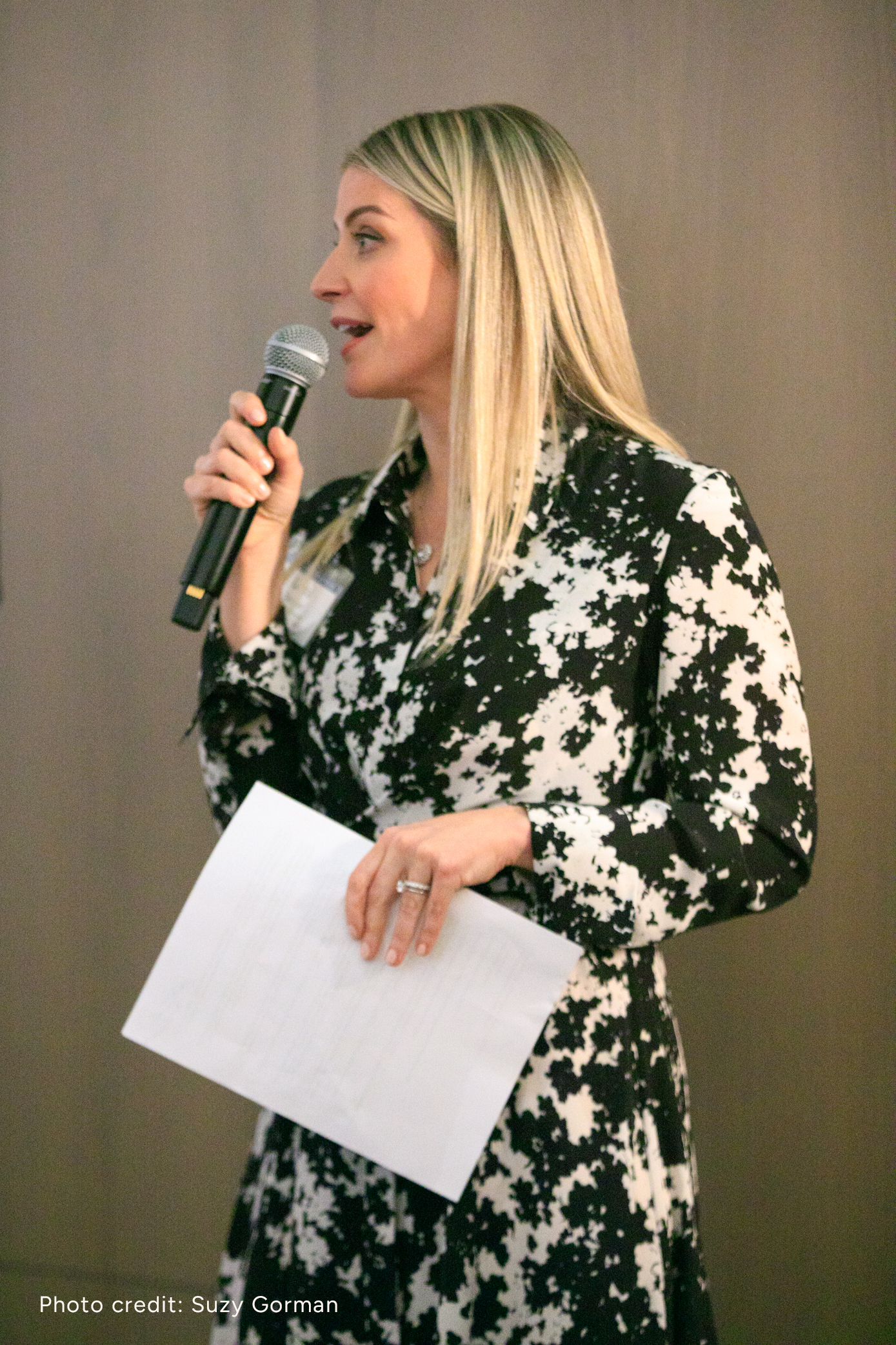 Laura K. Sawyier is speaking into a microphone while holding a sheet of paper.