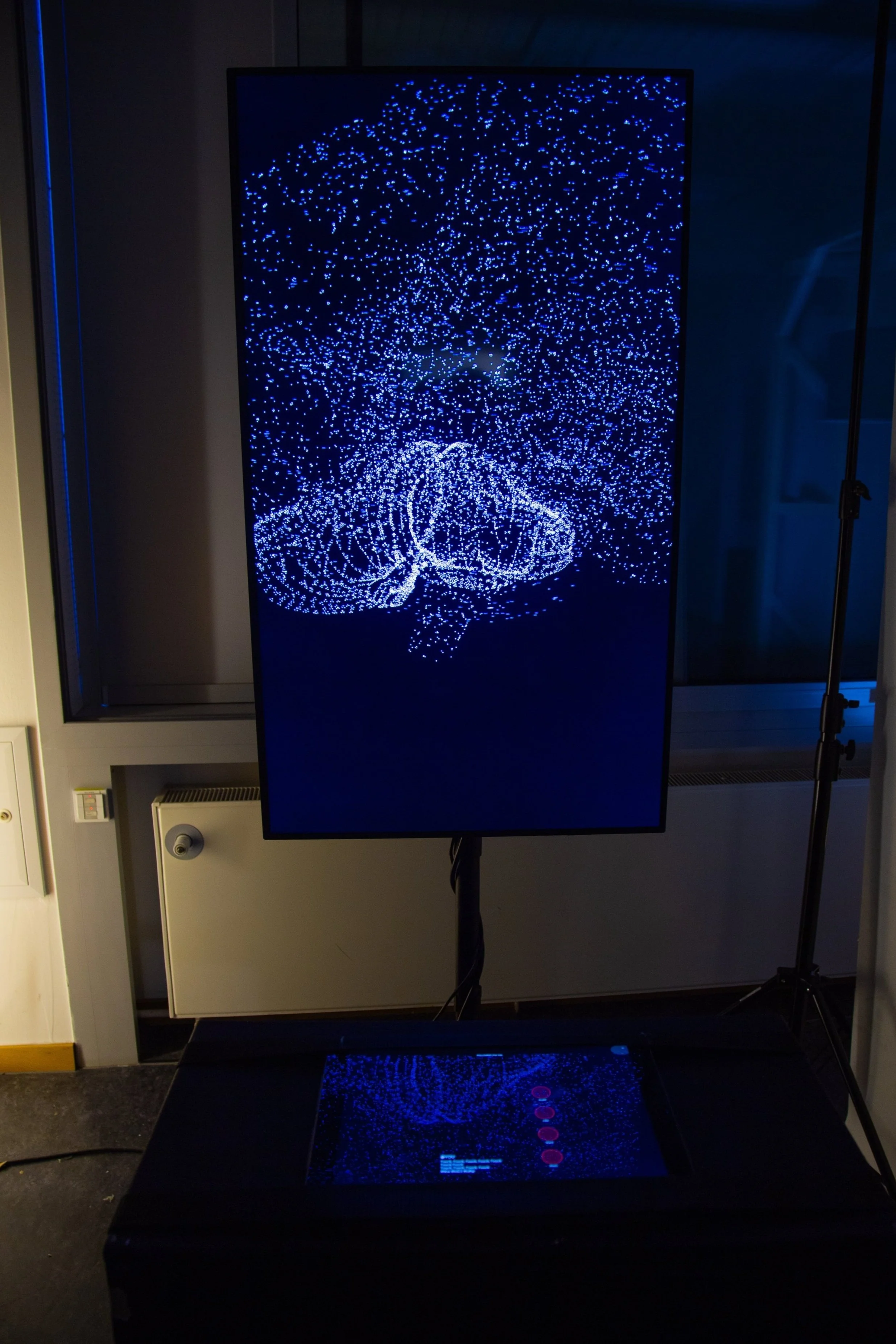 Ein vertikaler Bildschirm zeigt eine digitale Darstellung eines leuchtenden, blauen, wirbelnden Keim- oder Zellenmusters, das von oben betrachtet wird.