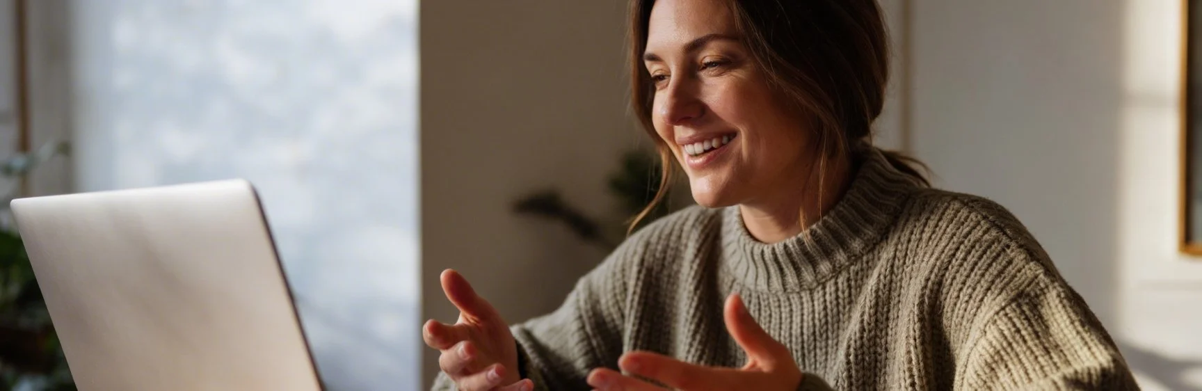 A woman smiling while having a video call on her laptop in a cozy indoor setting.