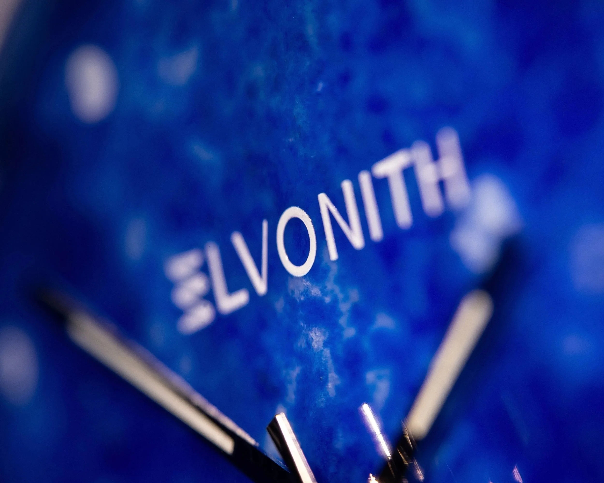 Nahaufnahme eines blauen Zifferblatts einer Uhr der Kollektion "NOCTIS" von der Marke 'ELVONITH', und zwei silberne Uhrzeiger.