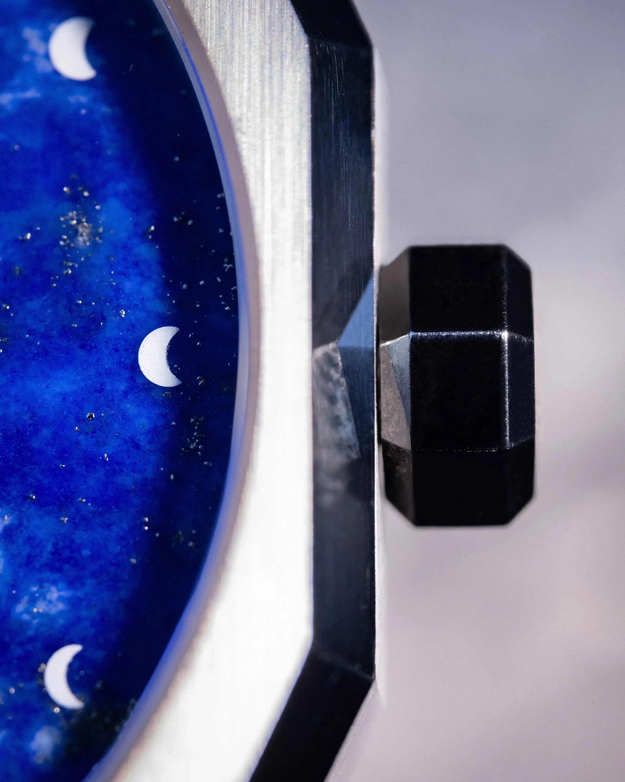 Nahaufnahme eines Zifferblattes einer ELVONITH Uhr mit einer astronomischen Darstellung der Indizes auf blauem Untergrund. Eine mehreckige Krone sitzt am Gehäuse