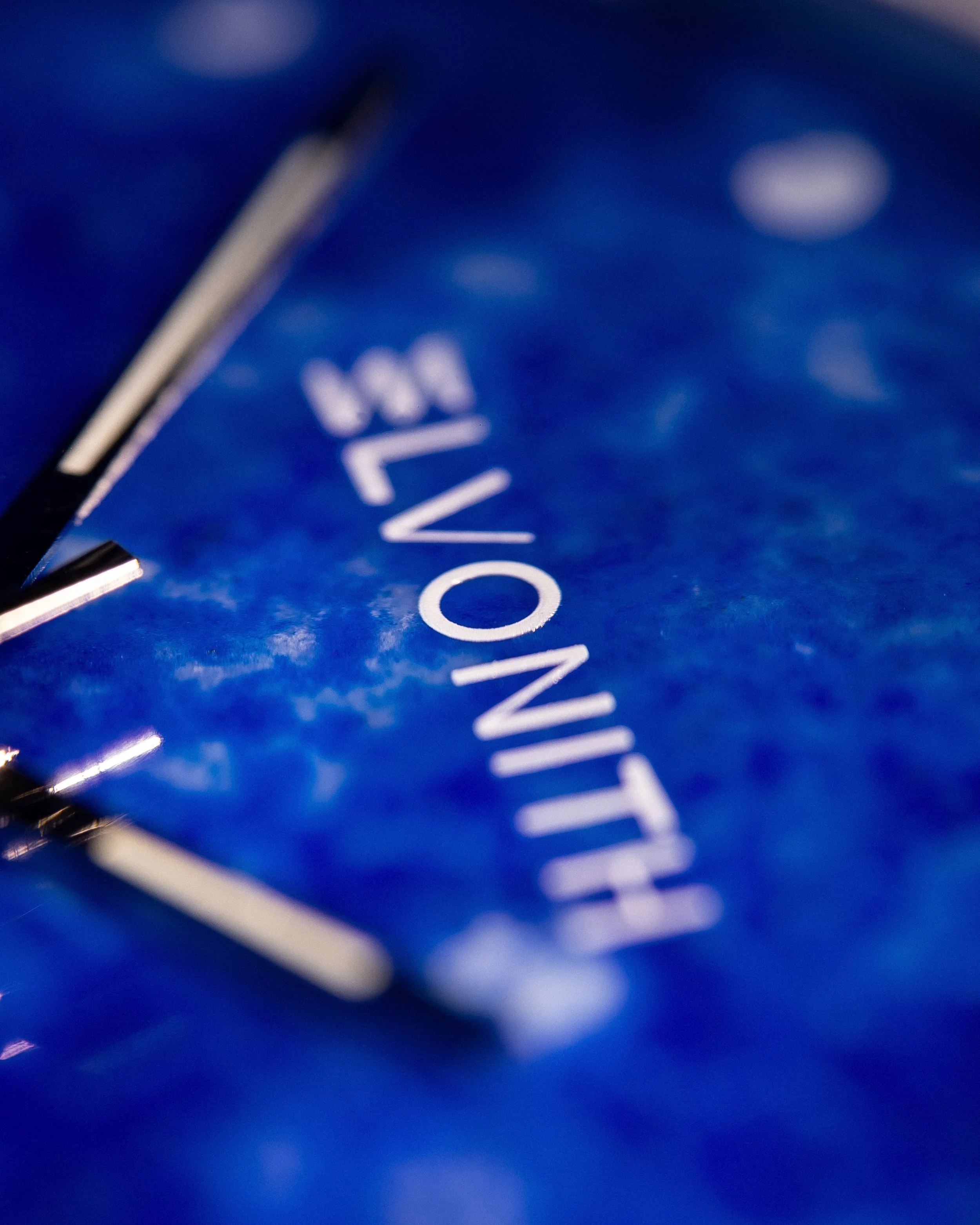 Nahaufnahme eines blauen Uhren-Zifferblattes mit weißer Schrift, teilweise sichtbar.