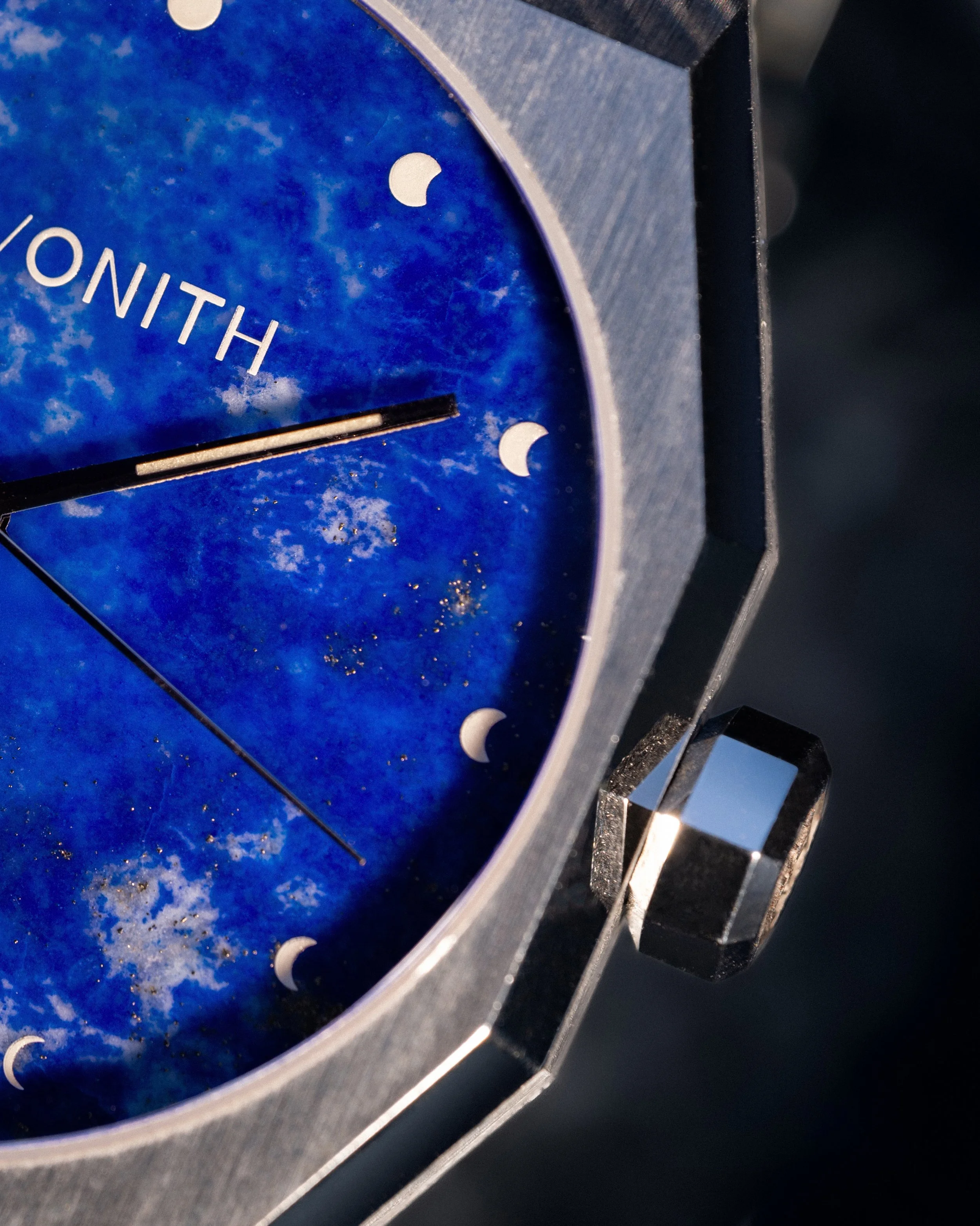 Nahaufnahme einer Uhr mit blauem, mondphasigem Zifferblatt und silbernem Gehäuse, Blick auf die rechte Seite der Uhr mit sichtbarer Krone.