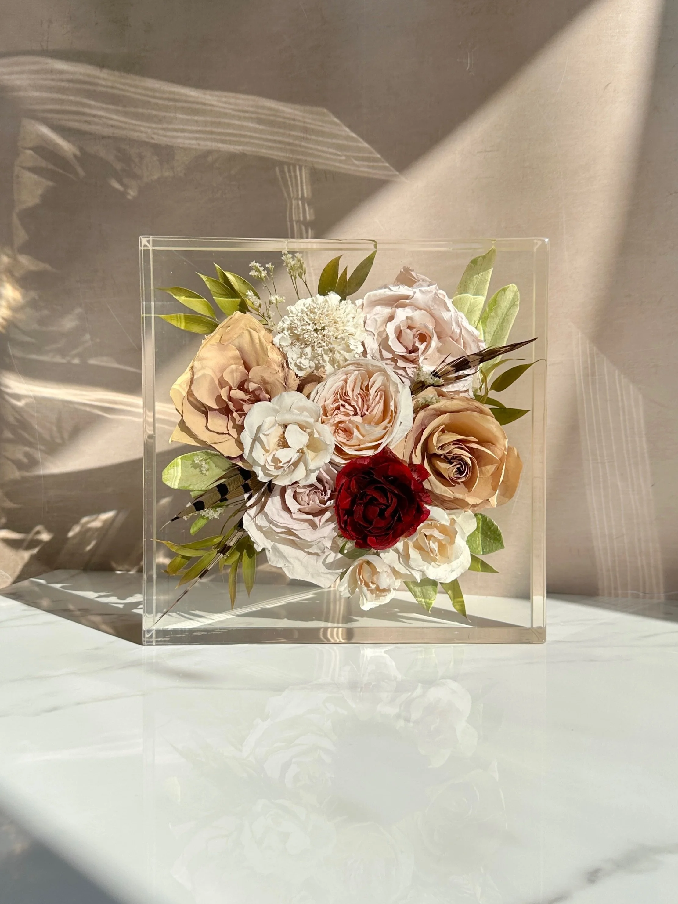 A fall bouquet, preserved exactly as it deserves to be. 🍂🤎

This 10&times;10 floral preservation block features a beautiful mix of warm neutrals, soft blush tones, deep burgundy, greenery, and the original feathers tucked throughout the bouquet. Ev