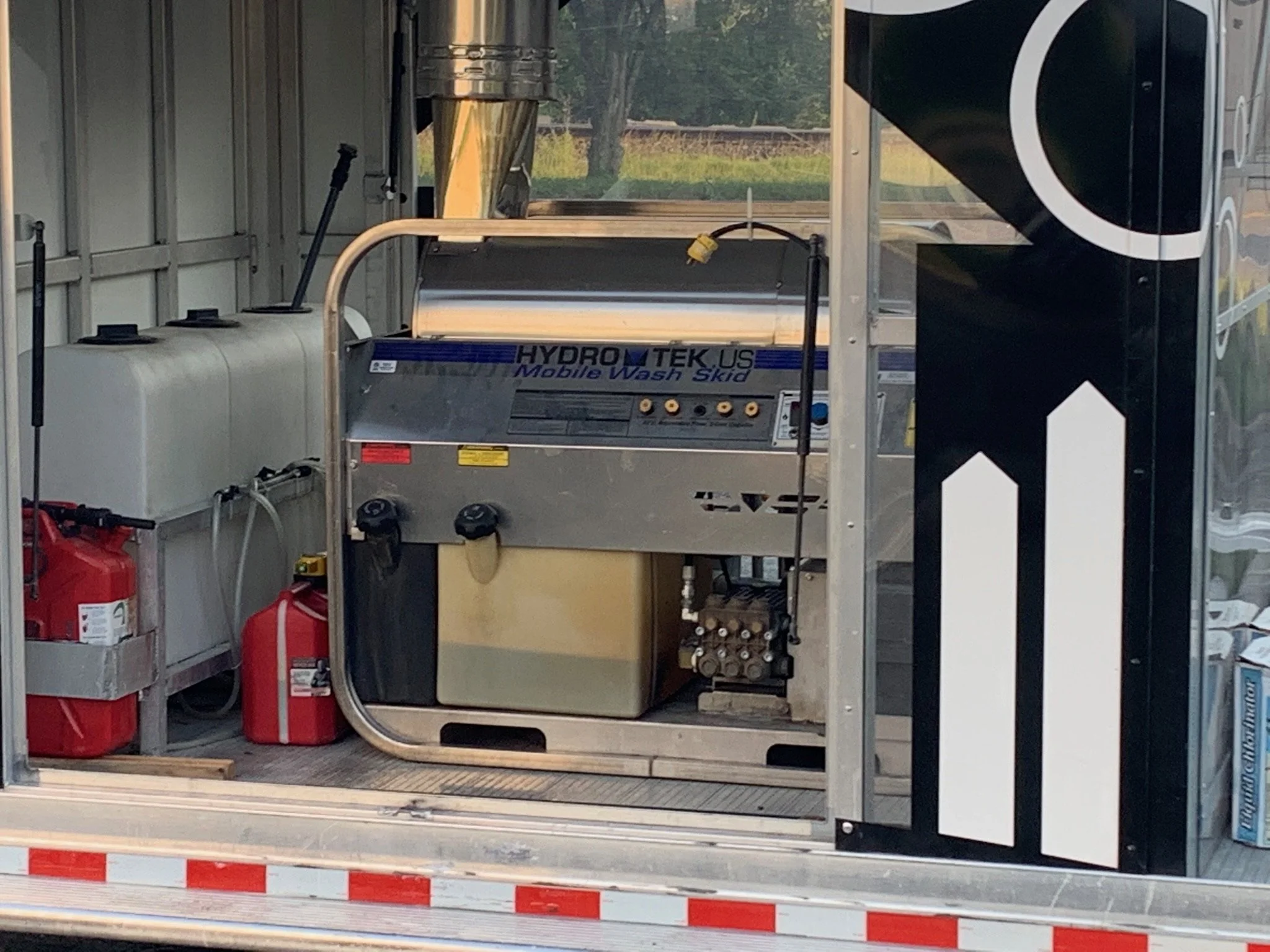 Mobile wash skid with water tanks and red fuel cans inside a vehicle or trailer.