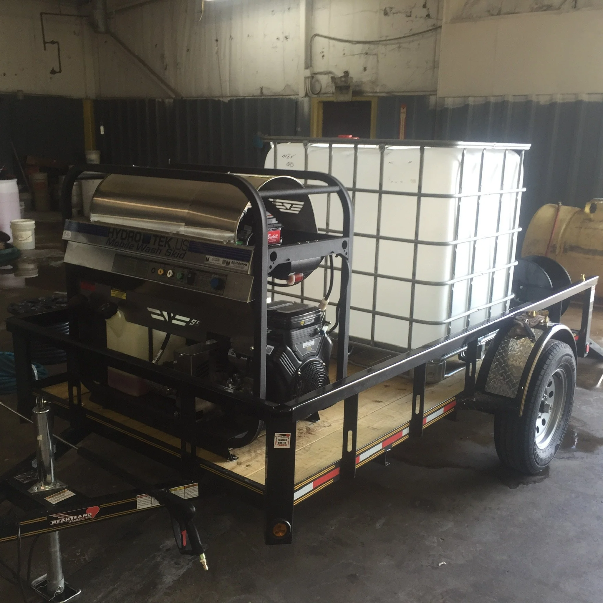 Mobile pressure washing trailer with Hydro Tek equipment and water tank inside a workshop.
