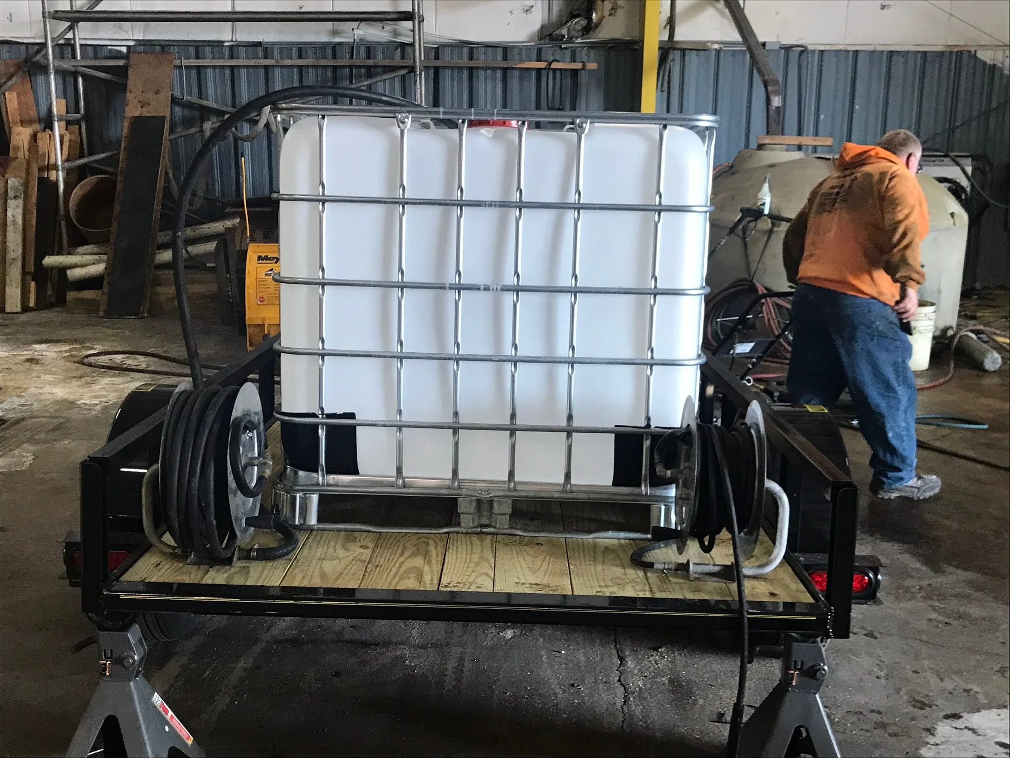 A large white water tank on a trailer in a workshop with a person in a hoodie nearby.