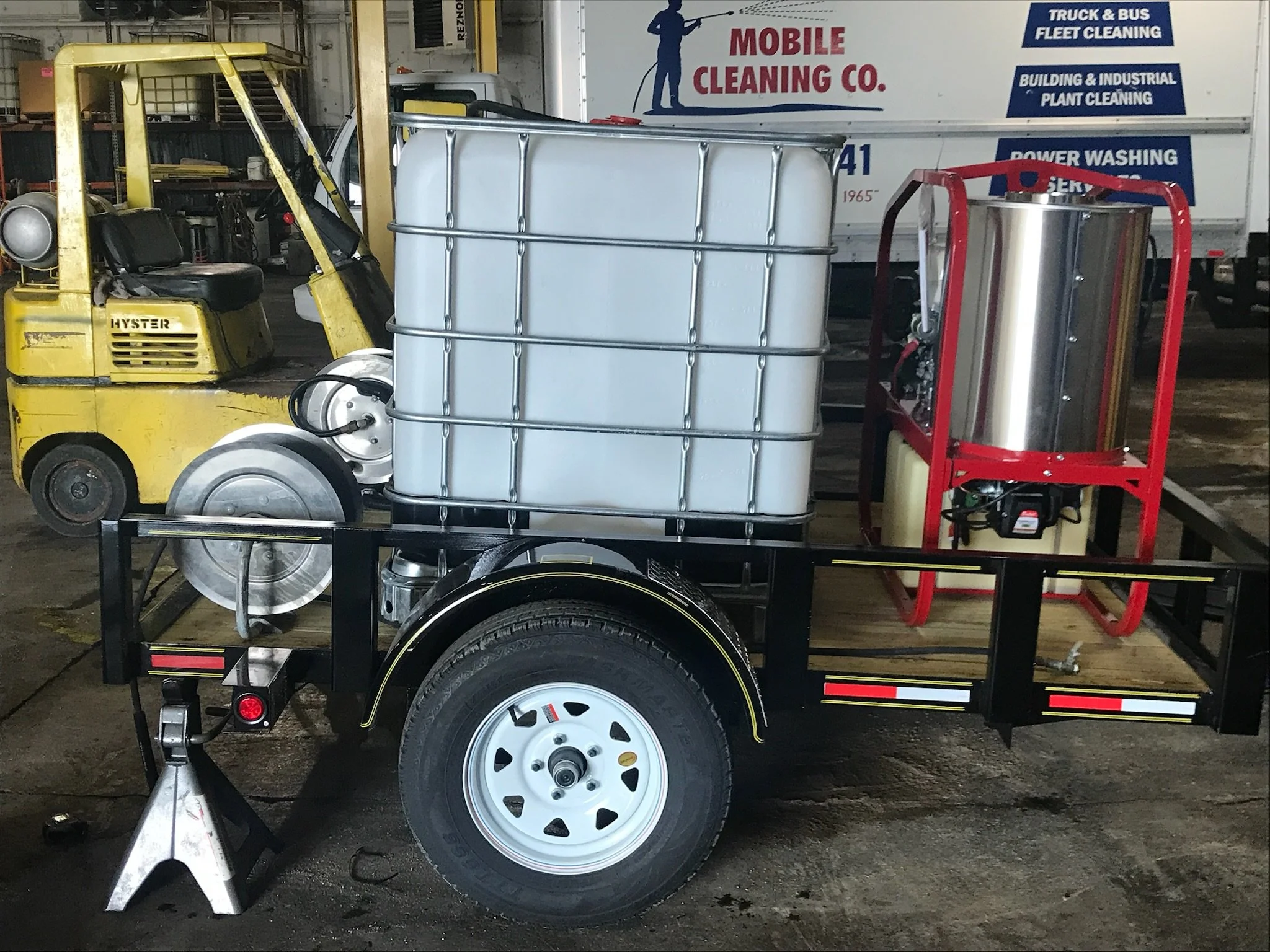 Mobile cleaning equipment on a trailer with a yellow forklift and white truck in a garage space.