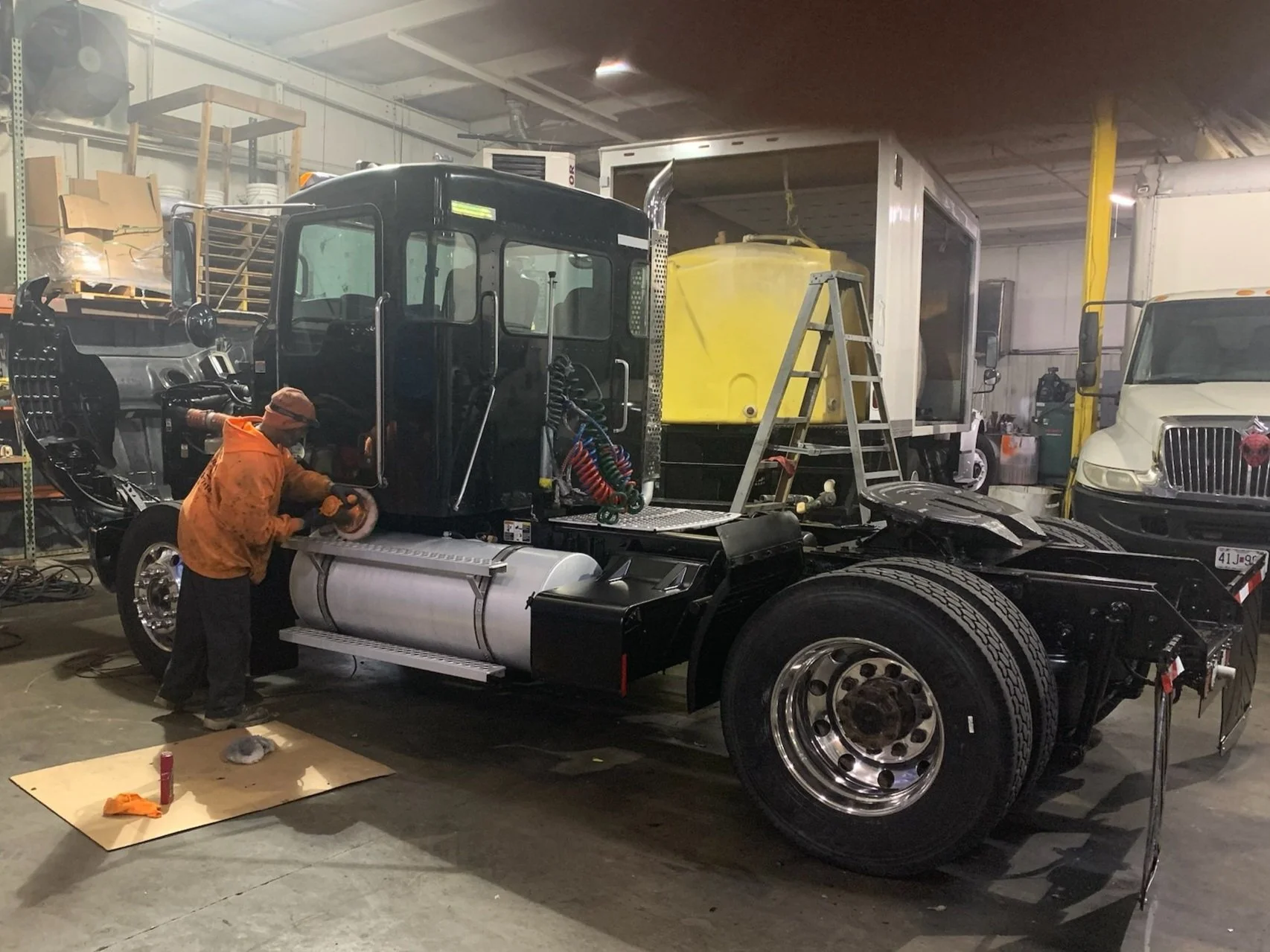 Person working on a truck inside a garage, using a tool on the vehicle's side.