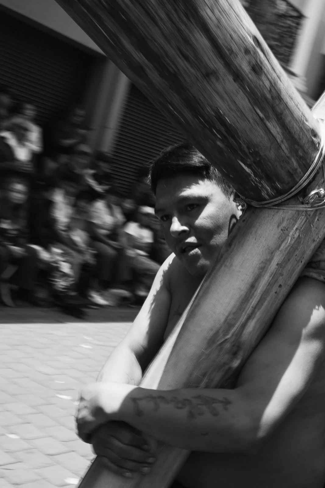 Un joven llevando un tubo grande en la calle, con un grupo de personas en el fondo