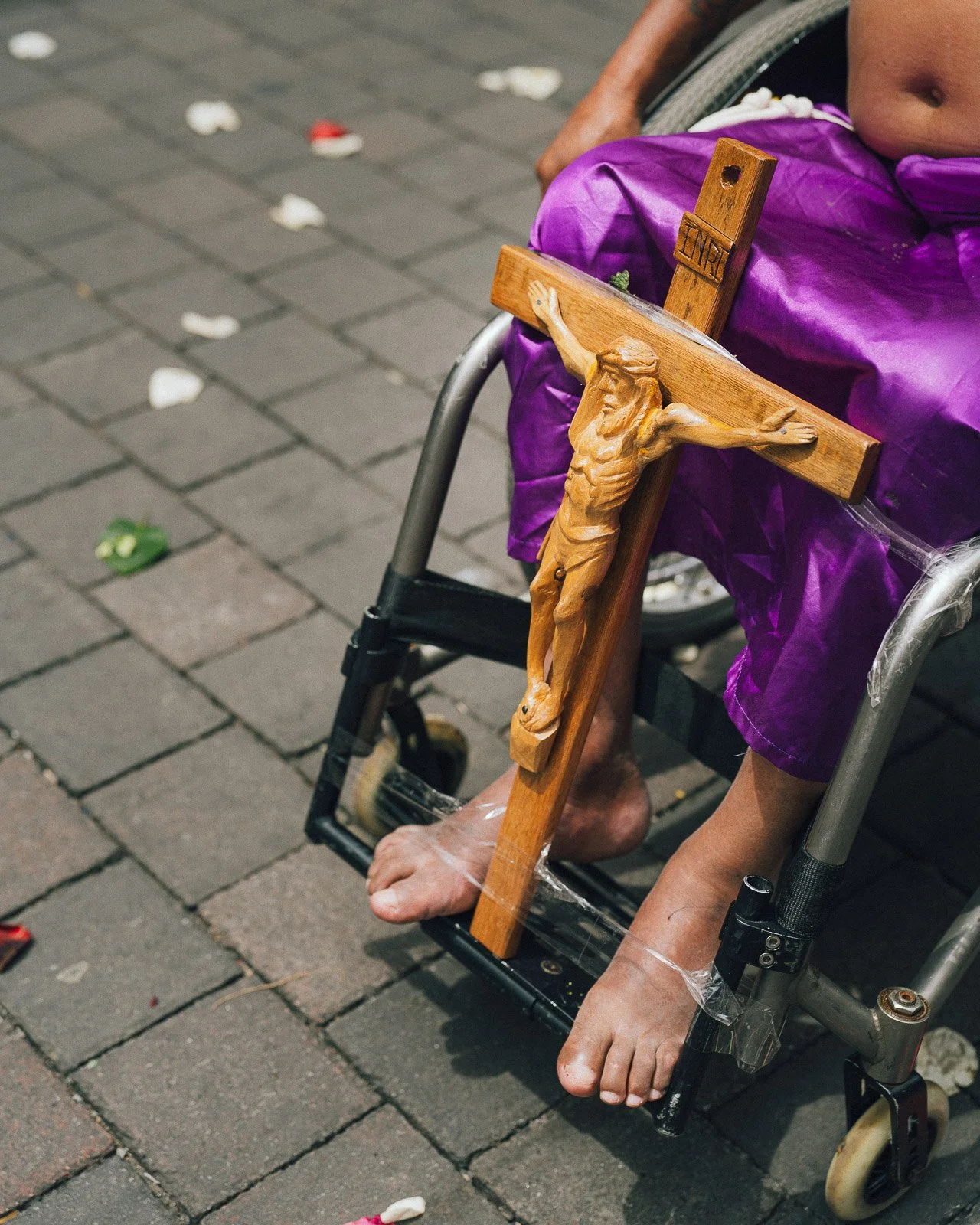 Crucifijo de madera, sostenido por pies de una persona en silla de ruedas con pantalones morados.
