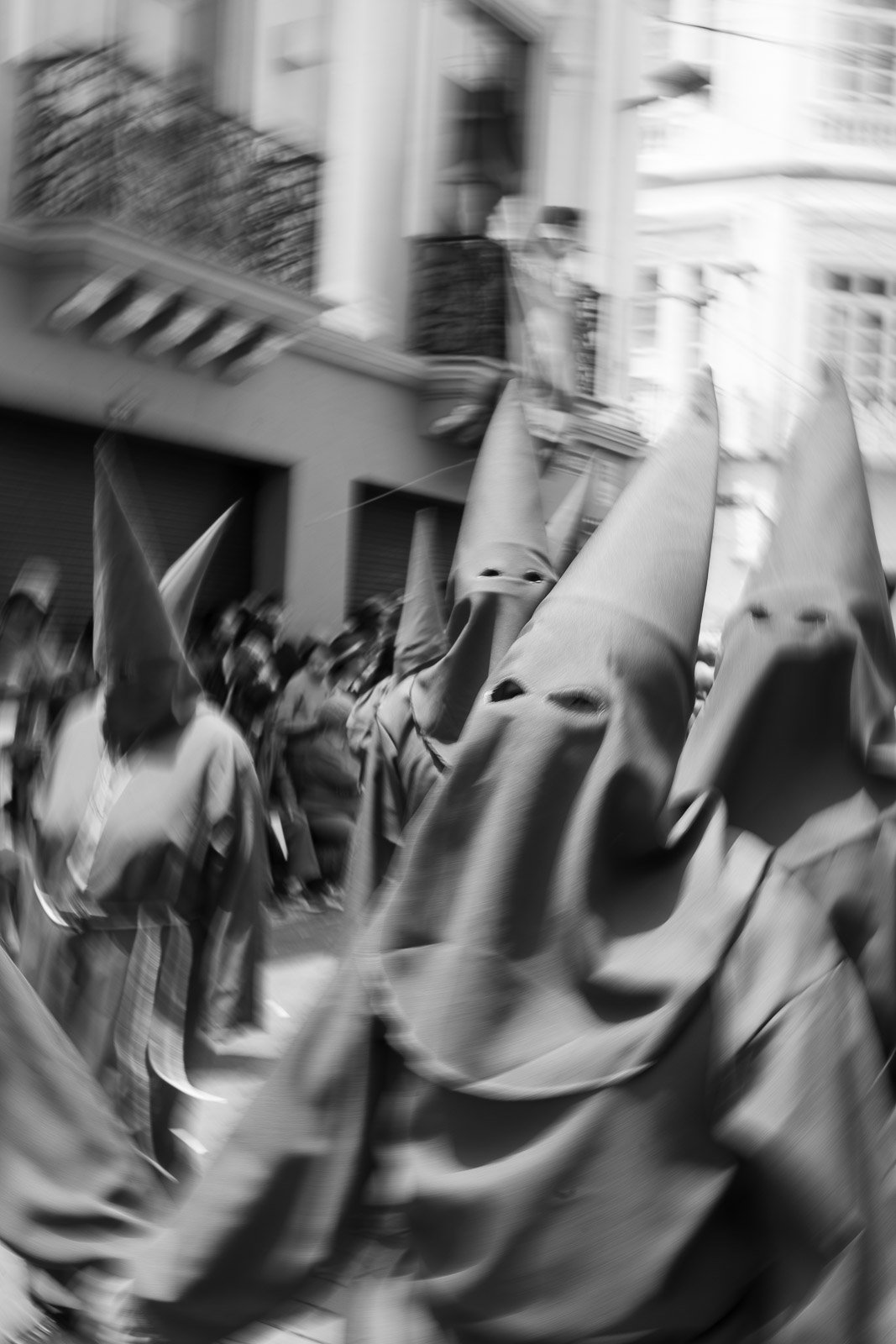 Personas en un desfile usando disfraces de capirote en una calle urbana