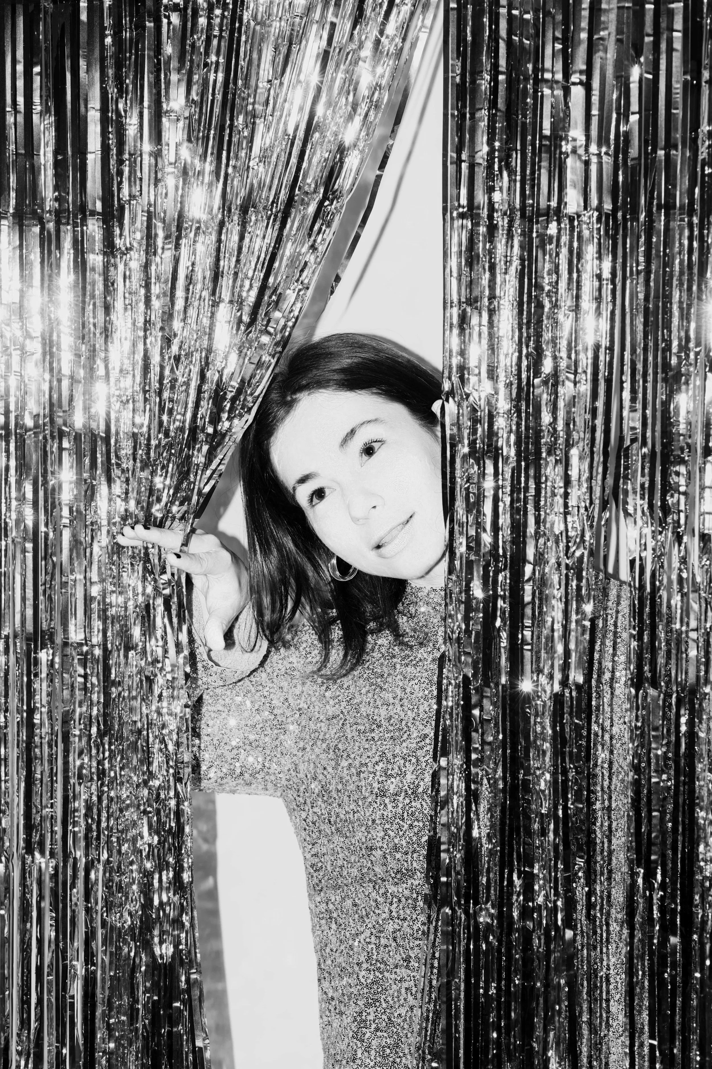 Mujer que espía por detrás de cortinas de hilos plateados.