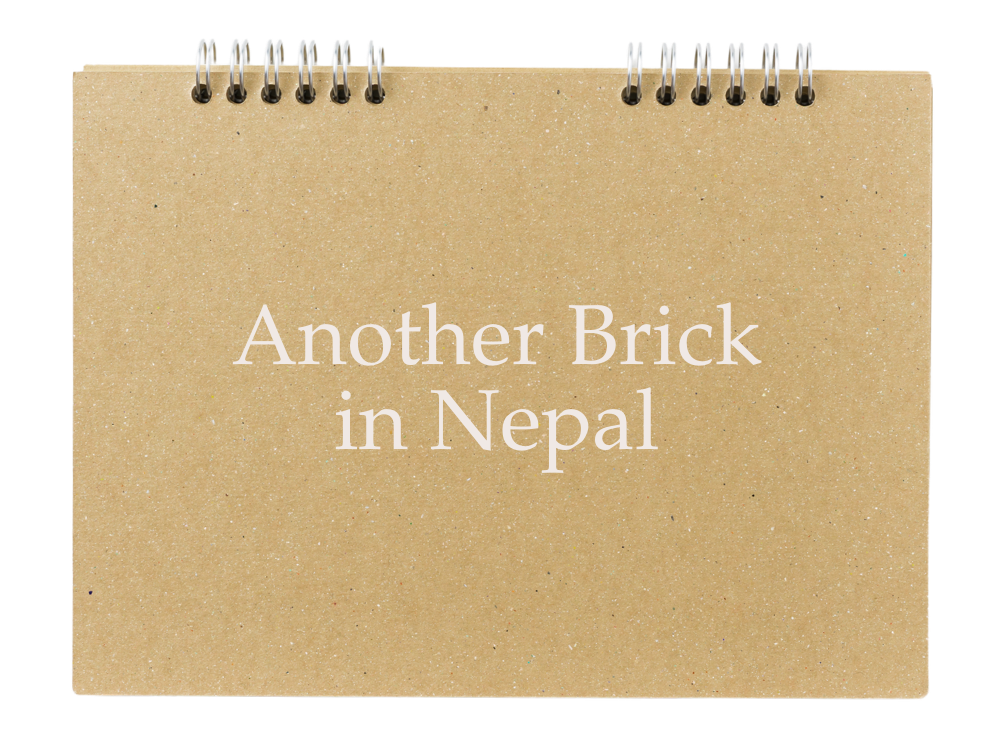 Brown spiral notebook with the text 'Another Brick in Nepal' on the cover.