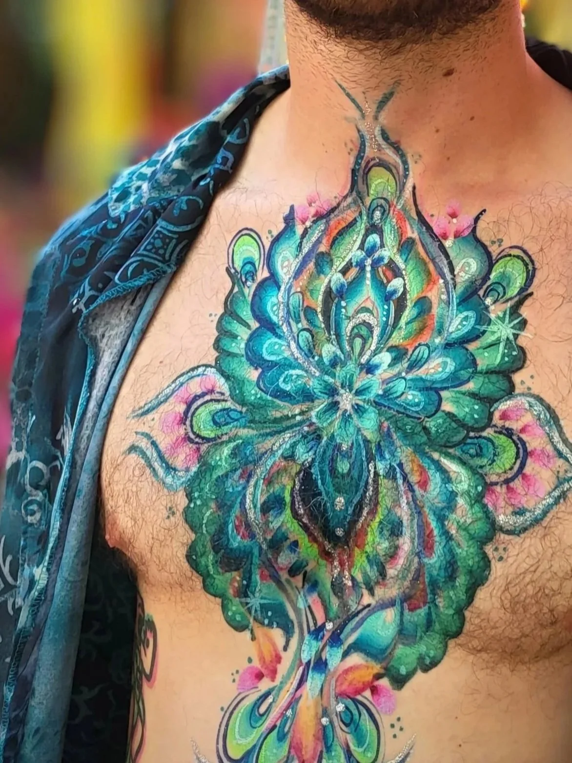 Colorful body art paint-design of a symmetrical, abstract floral design on a person's chest with a gradient of bright colors including blue, green, pink, and orange.