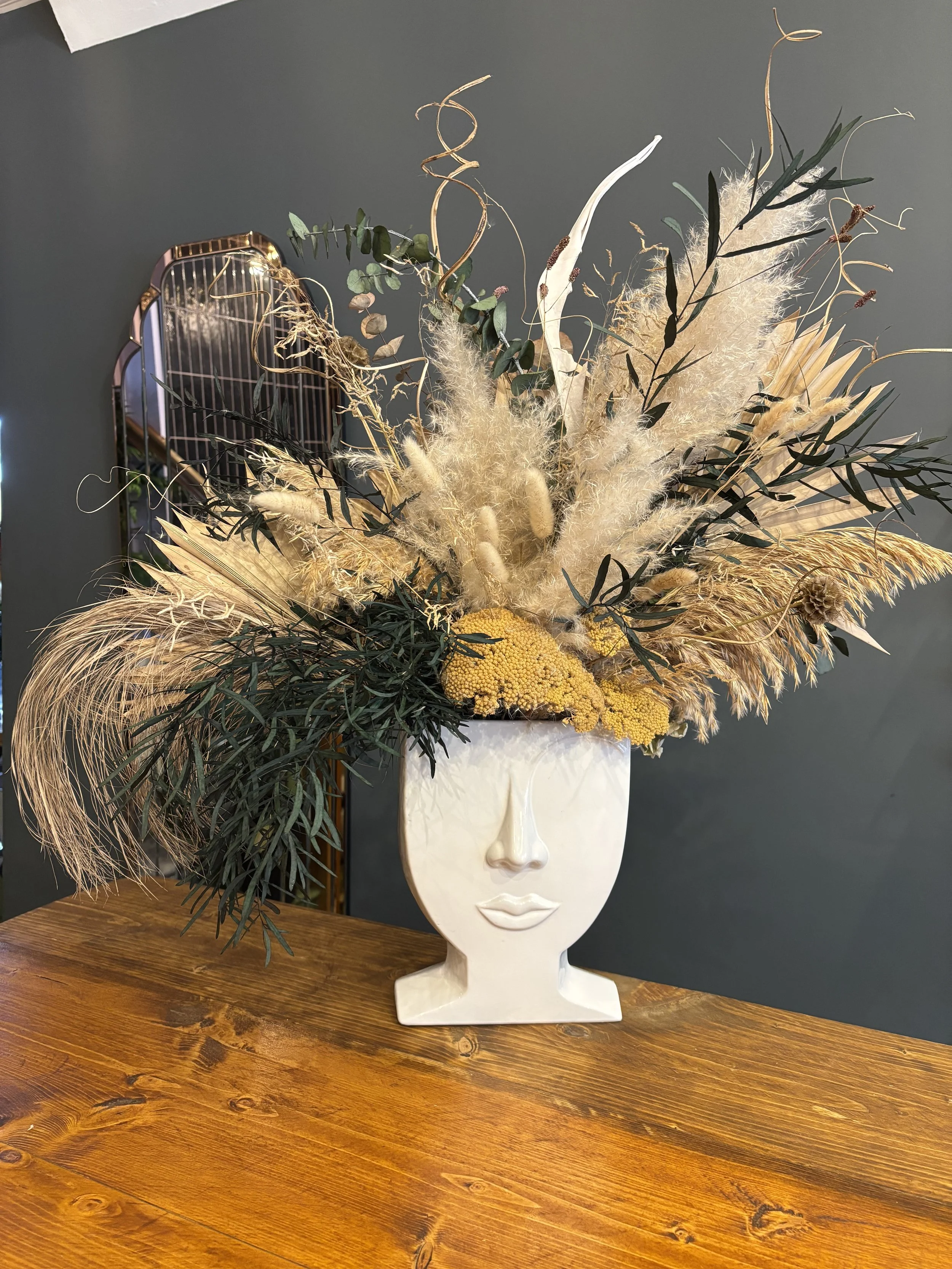 Decorative vase shaped like a human face with dried floral arrangement on top, featuring pampas grass, eucalyptus, and other dried botanicals.
