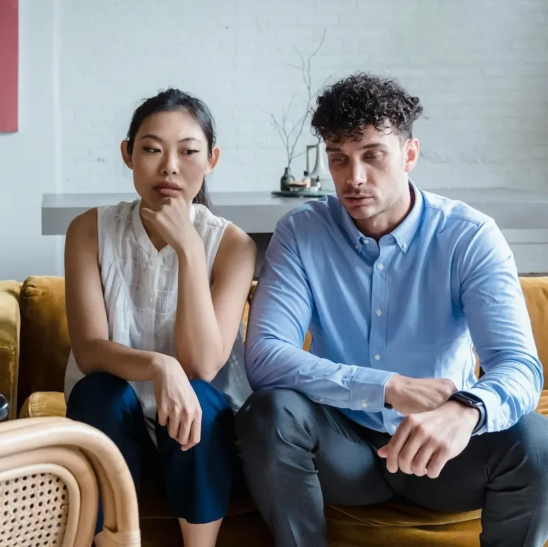 couple sitting together on sofa looking sad