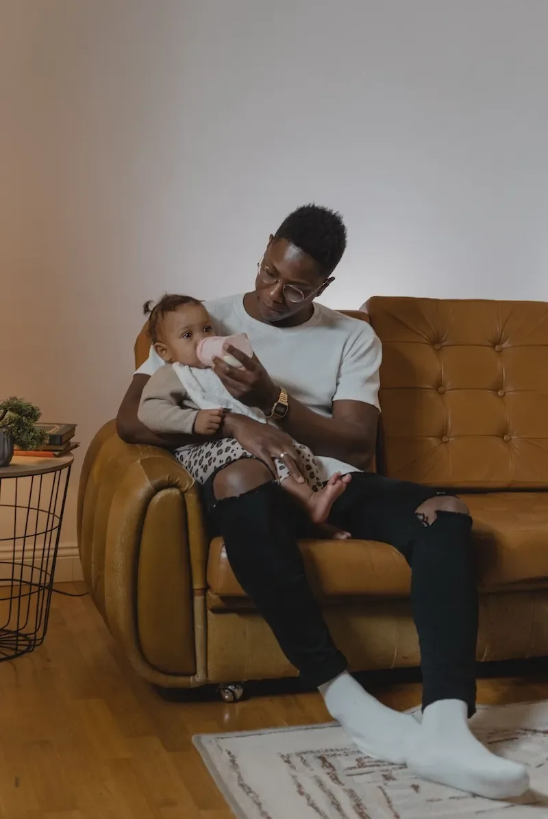 father feeding bottle to baby on sofa