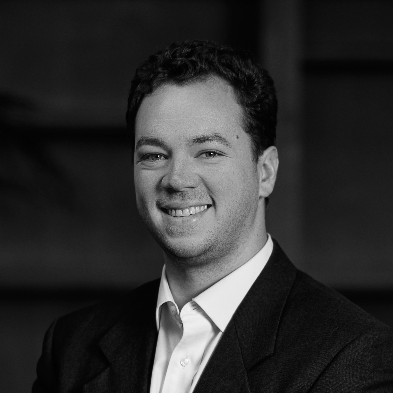 Black and white professional headshot of a smiling young man wearing a suit and white shirt.