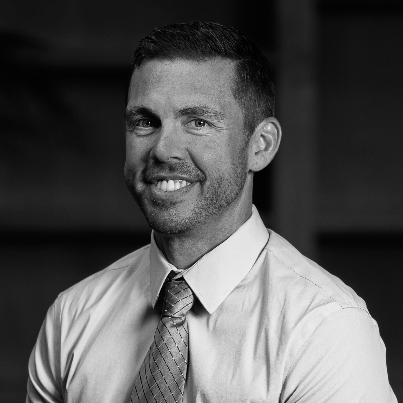 Black and white portrait of a man in a dress shirt and tie, smiling.