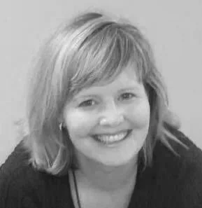 Black and white portrait of a smiling woman with long, wavy hair, wearing a button-up shirt and a dangling earring.