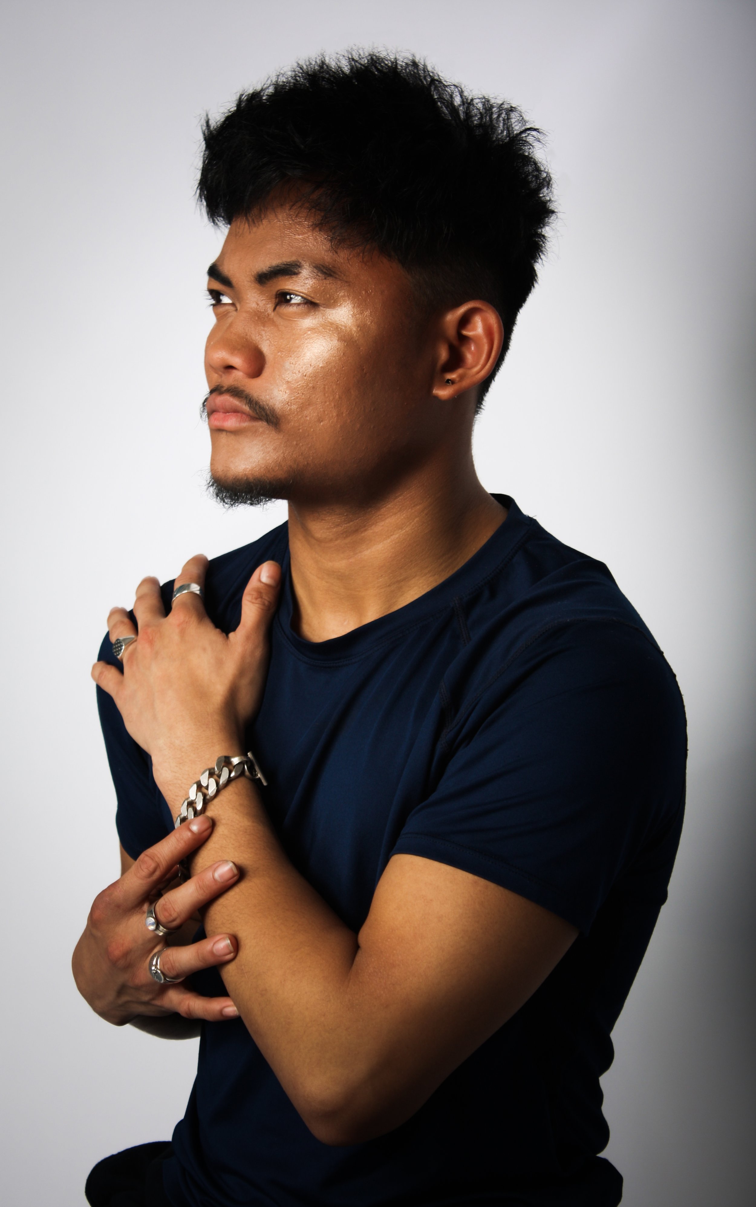 Man with short hair and a goatee, wearing a dark T-shirt, posing with his hands on his shoulder